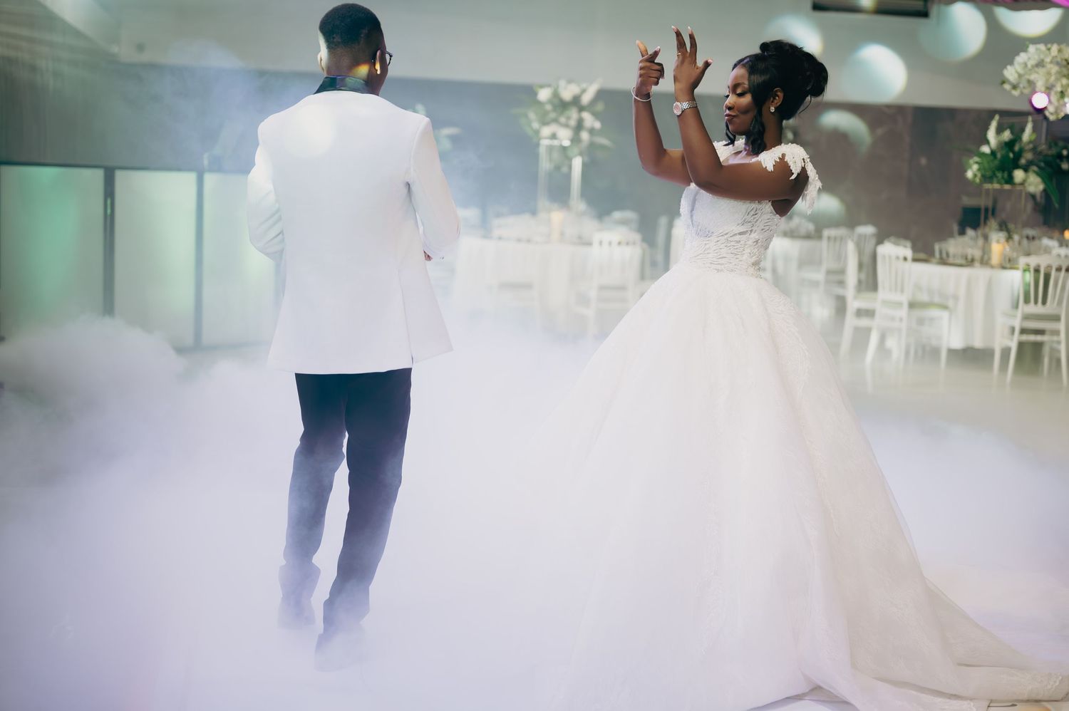 Bride and groom share first dance surrounded by dramatic fog on wedding reception dance floor.