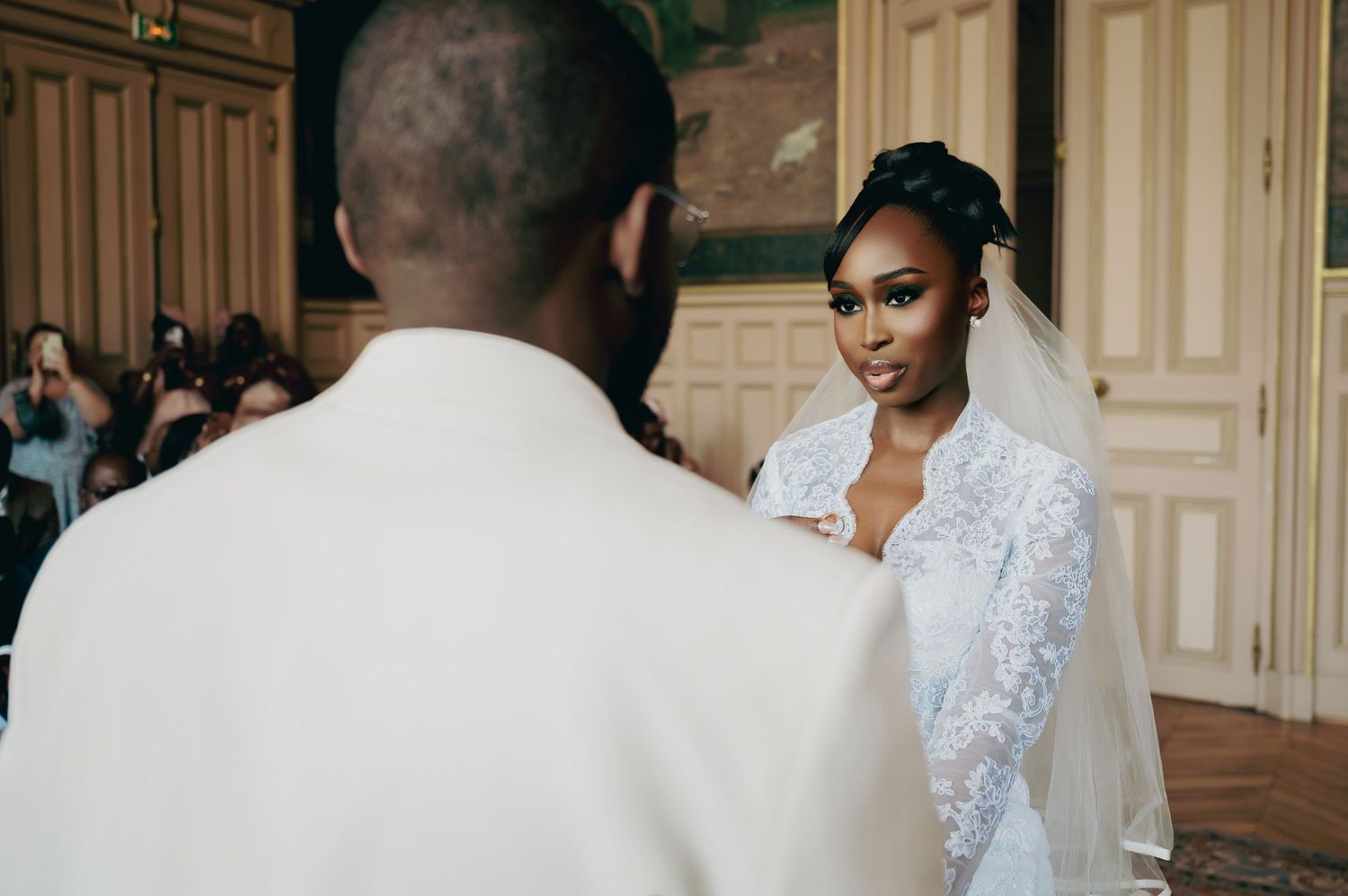 Bride in lace veil gazes at groom during intimate wedding ceremony exchange.