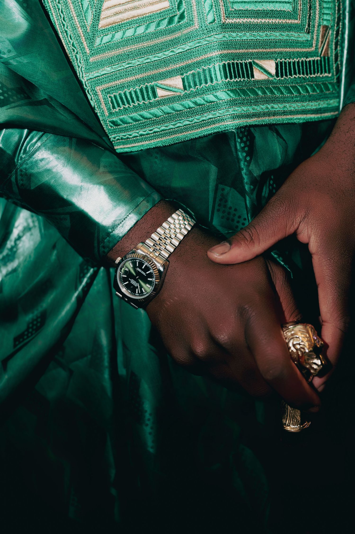 Close-up of hands in green African traditional attire adorned with a Rolex watch and gold ring.