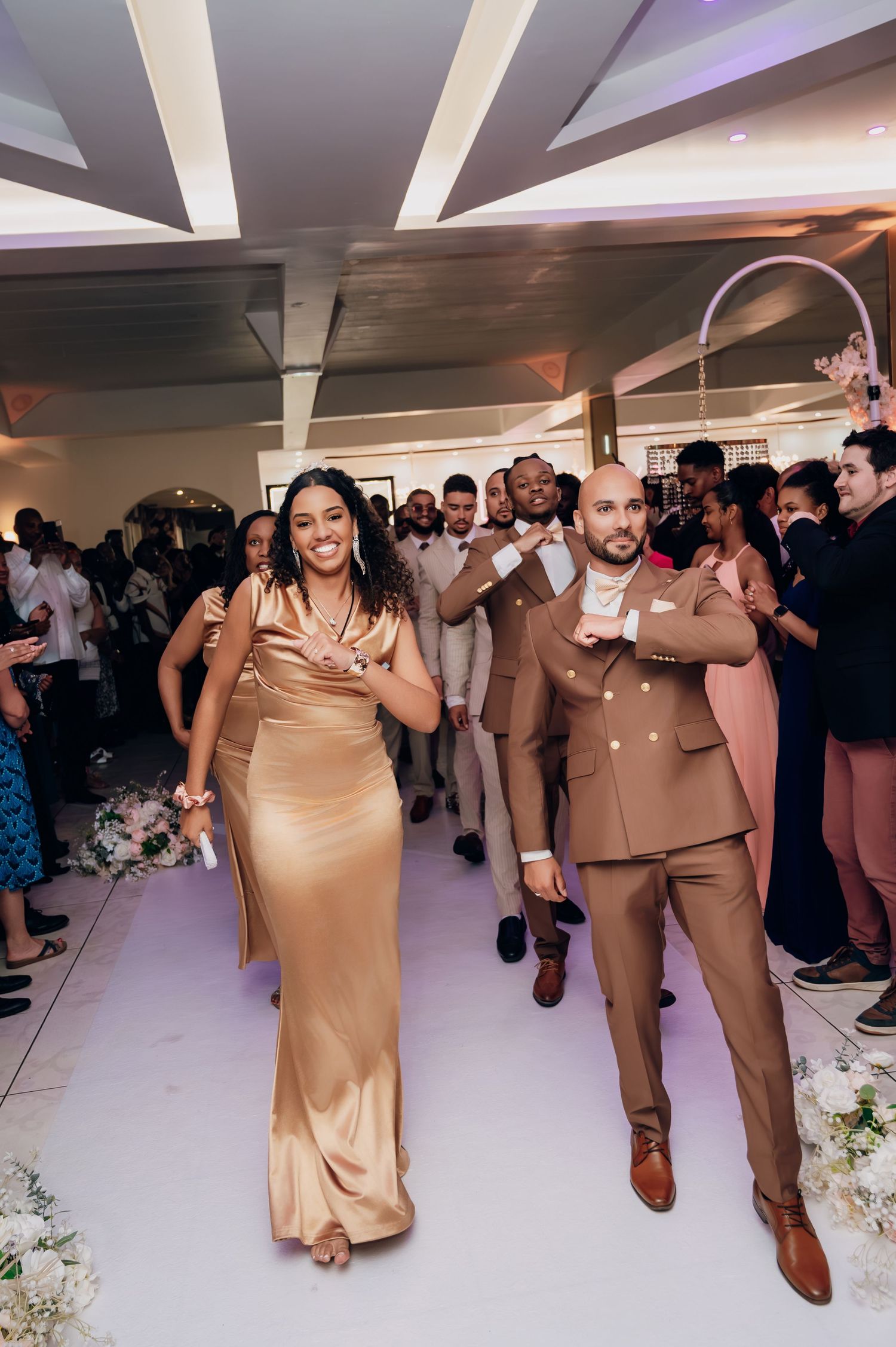 Bride and groomsman in gold and brown attire dancing at a wedding reception.