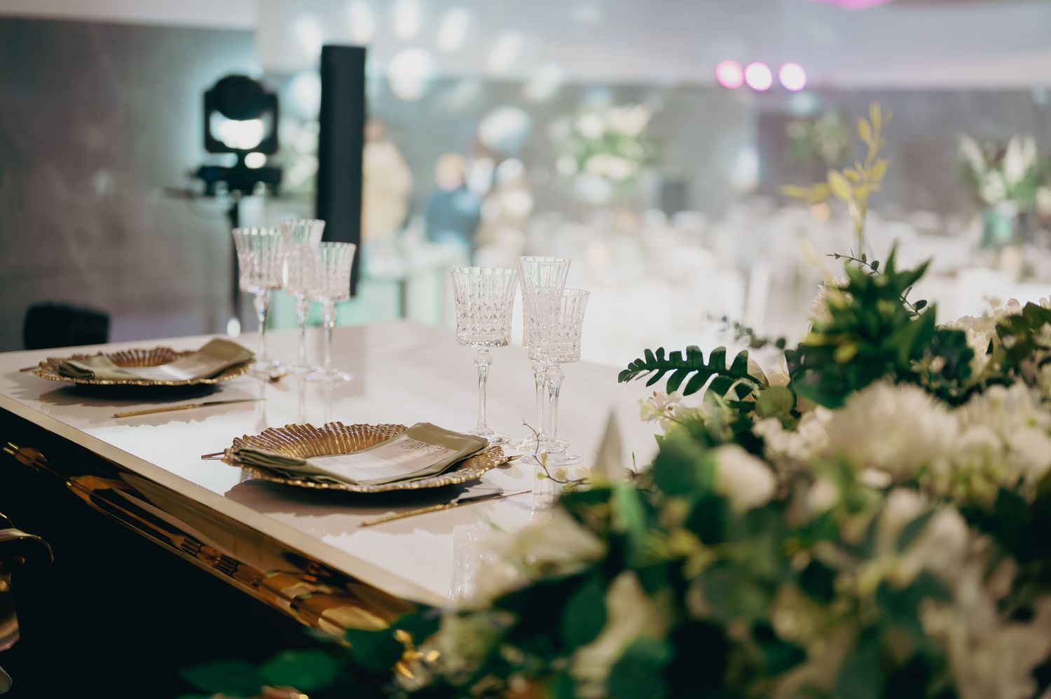 Sophisticated wedding table setting with gold charger plates, crystal glasses, and green foliage.