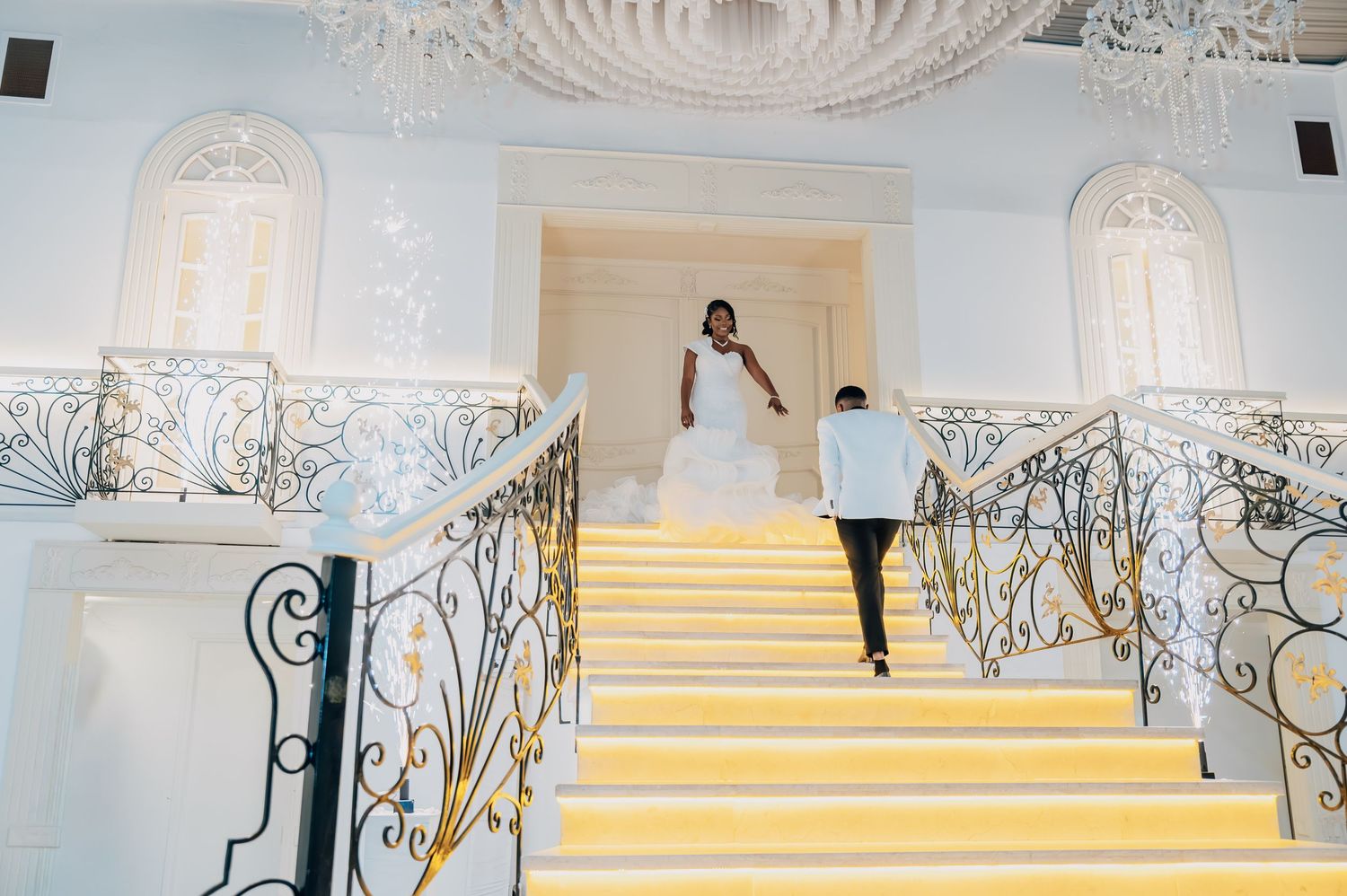 Bride and groom descend an elegant staircase with gold steps and wrought iron railings in a luxury venue.
