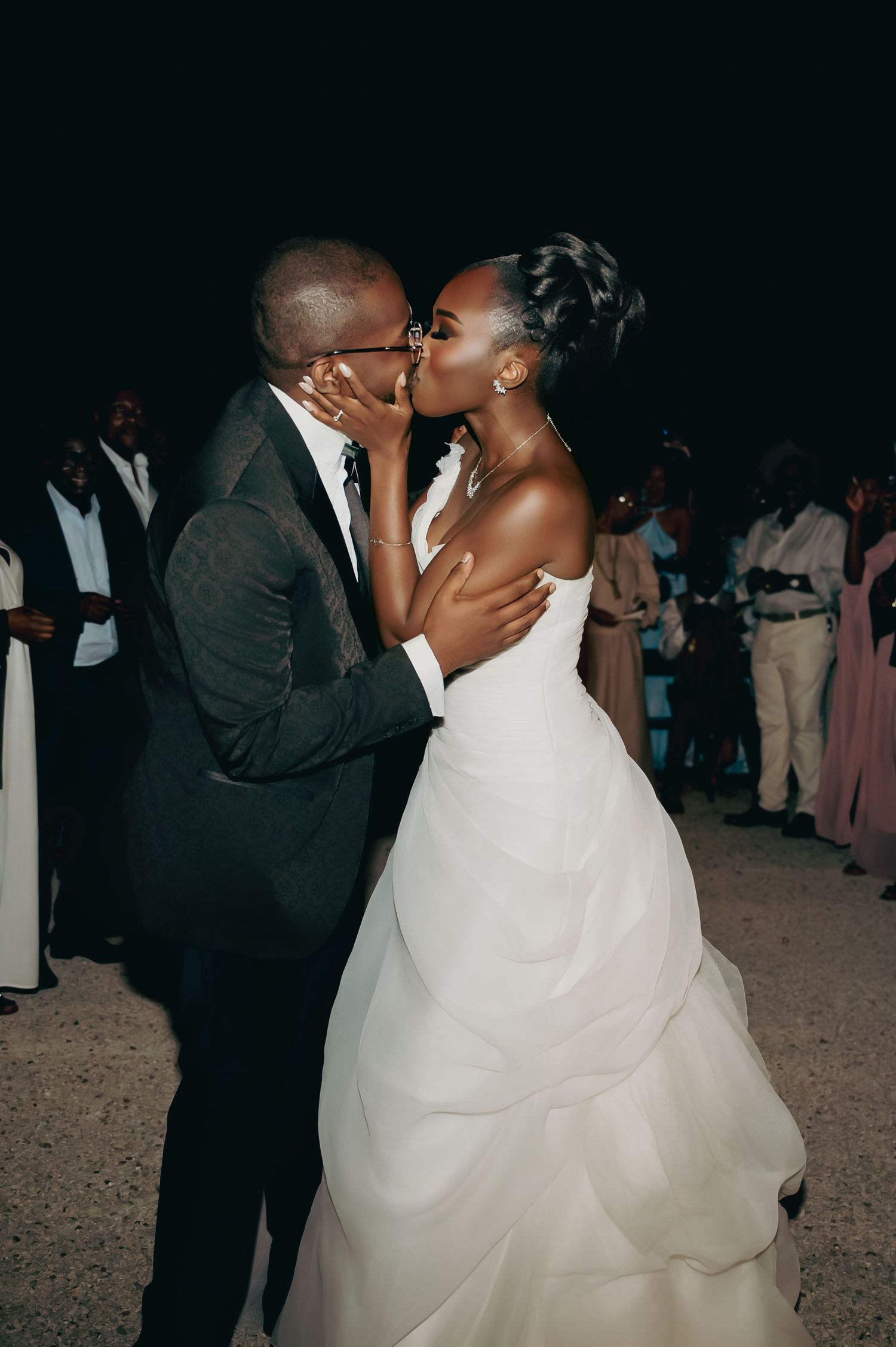 Bride and groom share romantic first kiss during outdoor nighttime wedding reception celebration.