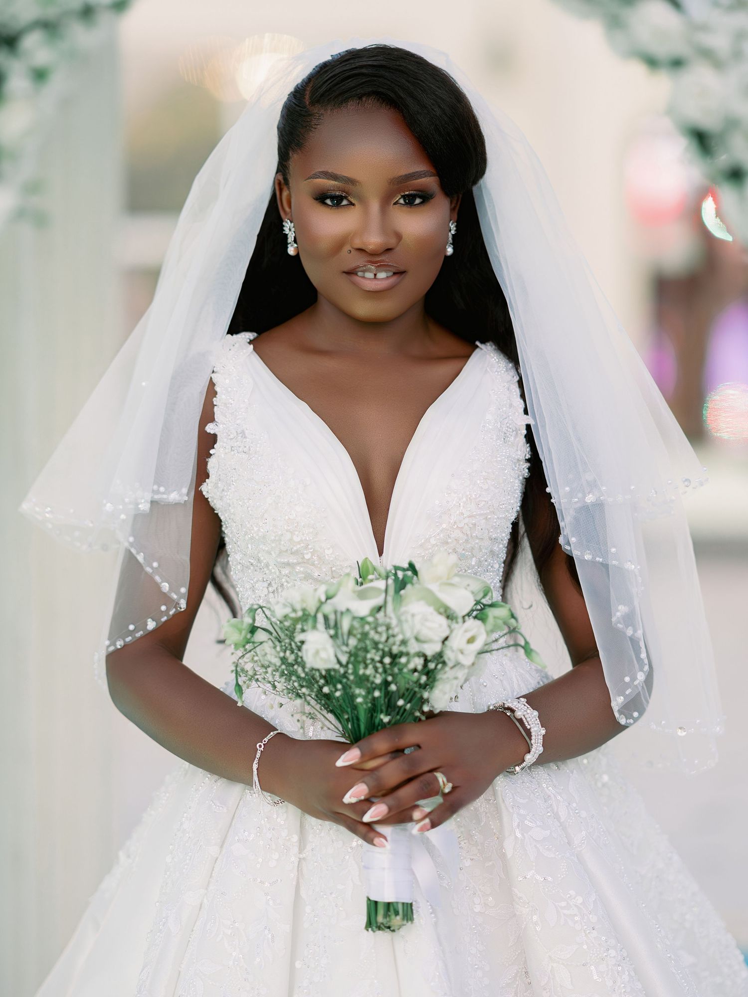 Elegant Black bride in a beaded V-neck ball gown with veil holding white floral bouquet.