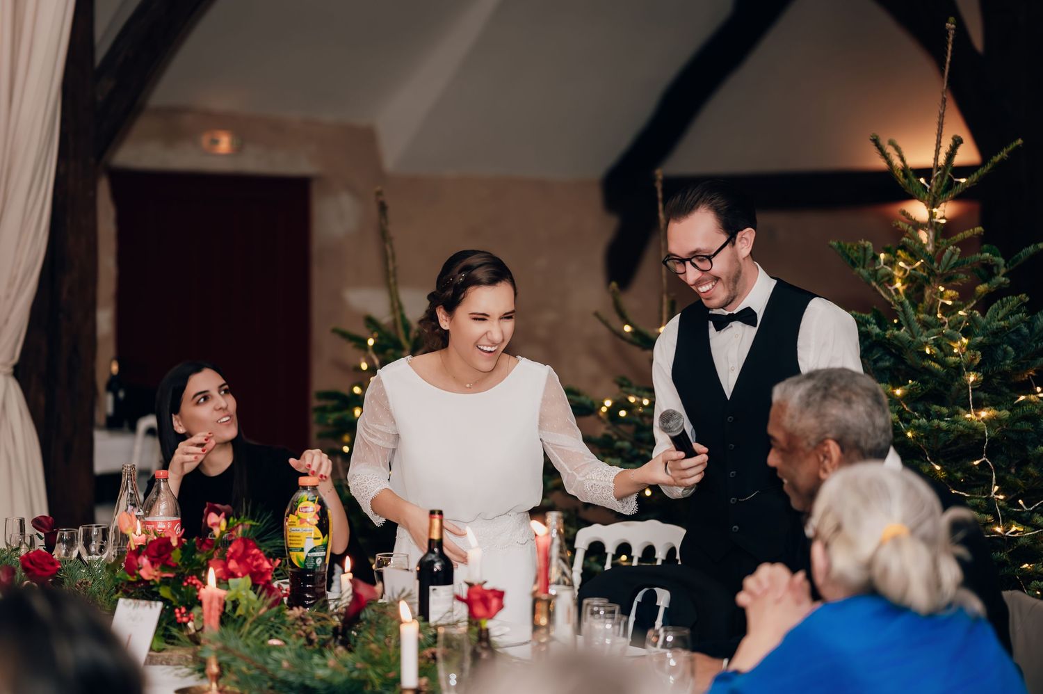 Bride and groom laughing with guests at decorated Christmas wedding reception dinner table.