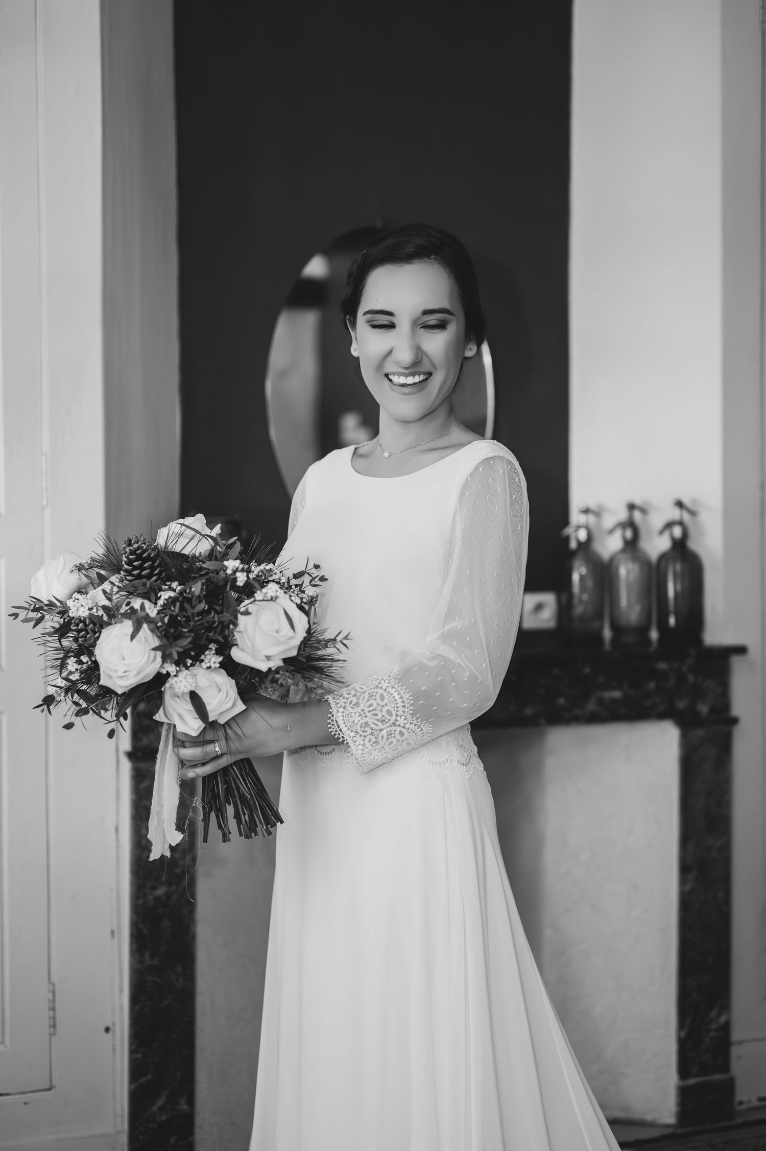 Black and white portrait of a laughing bride in white gown holding a floral bouquet.