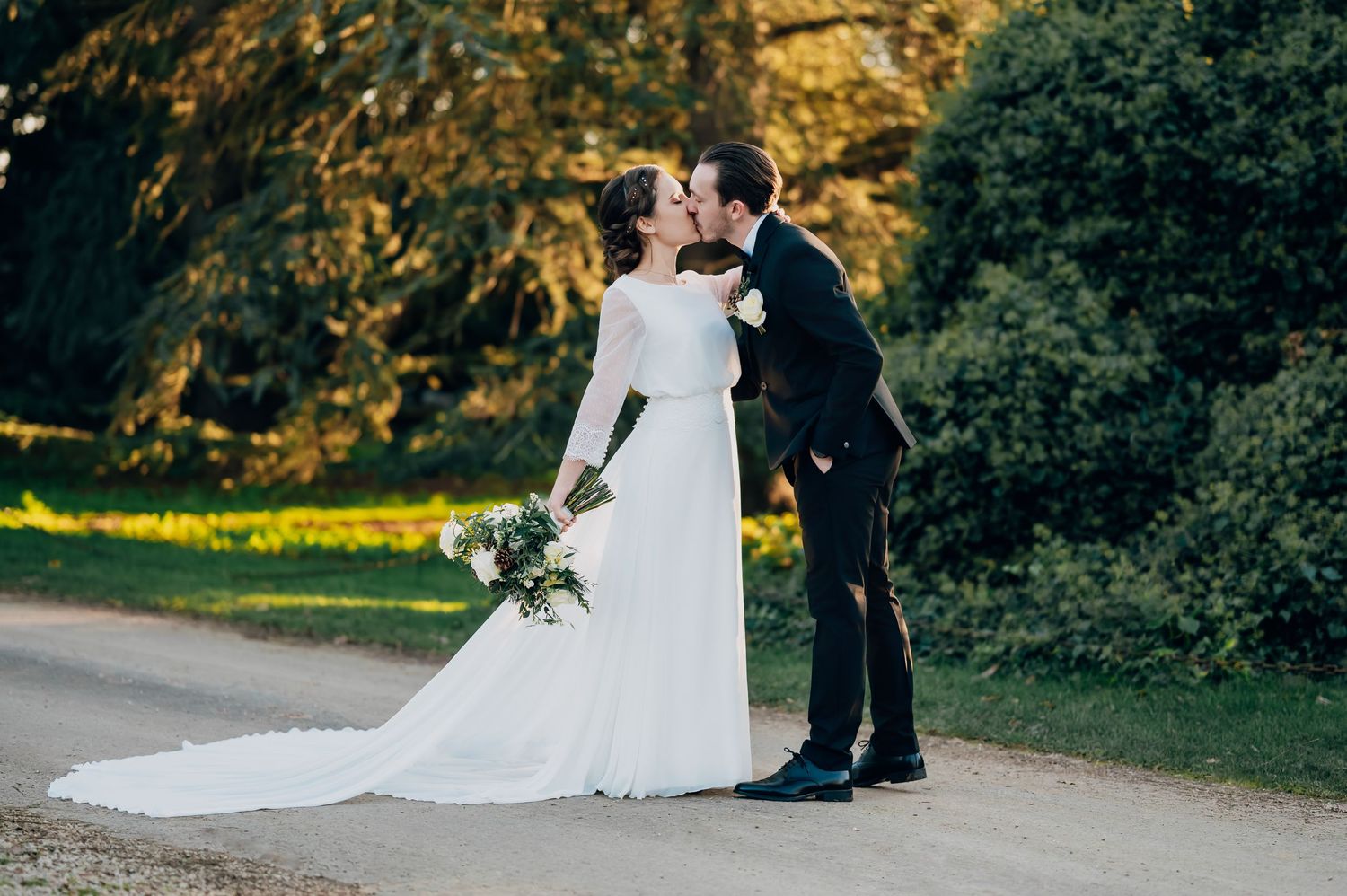 Bride and groom sharing a romantic kiss on a sunlit garden path at their outdoor wedding.