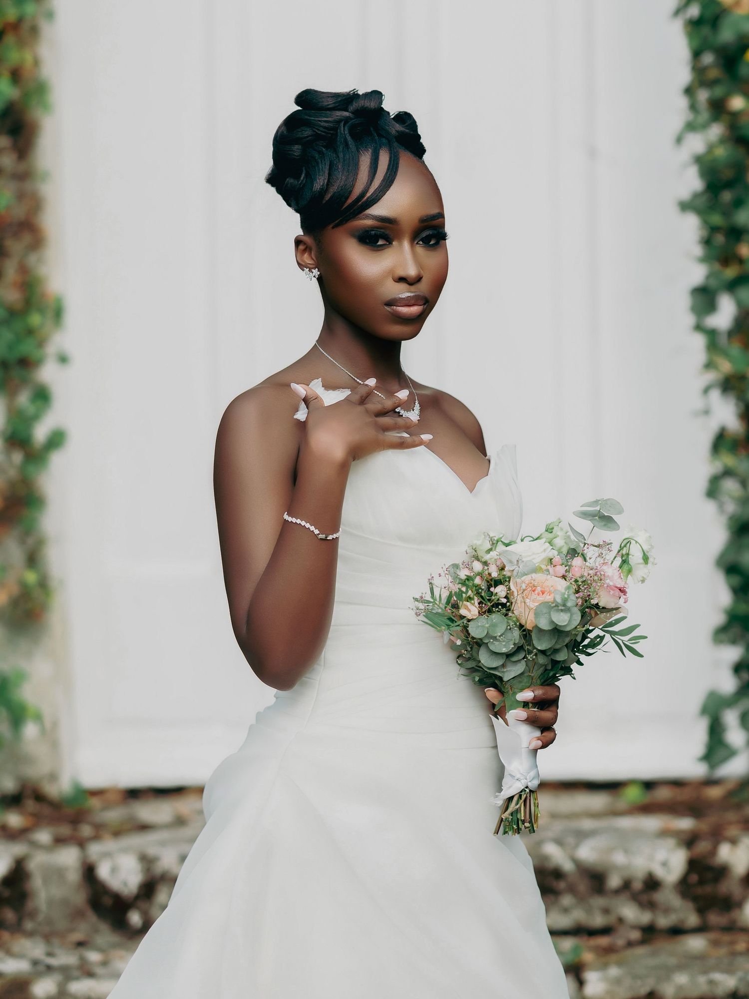 Stunning Black bride in white gown holds a pastel bouquet, adorned with butterfly hair accessories.