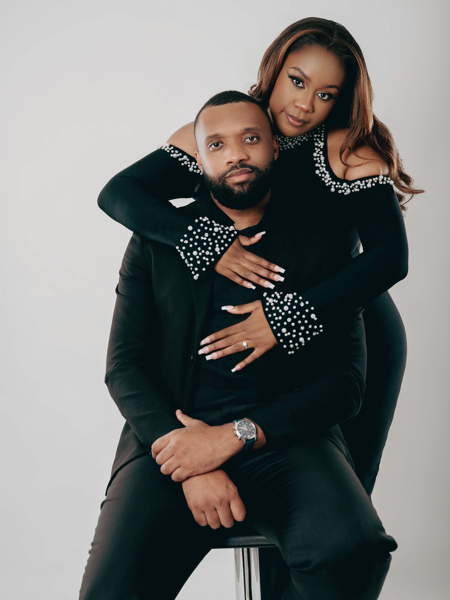 Romantic couple in black pearl-embellished outfits embracing during a studio engagement photo session.