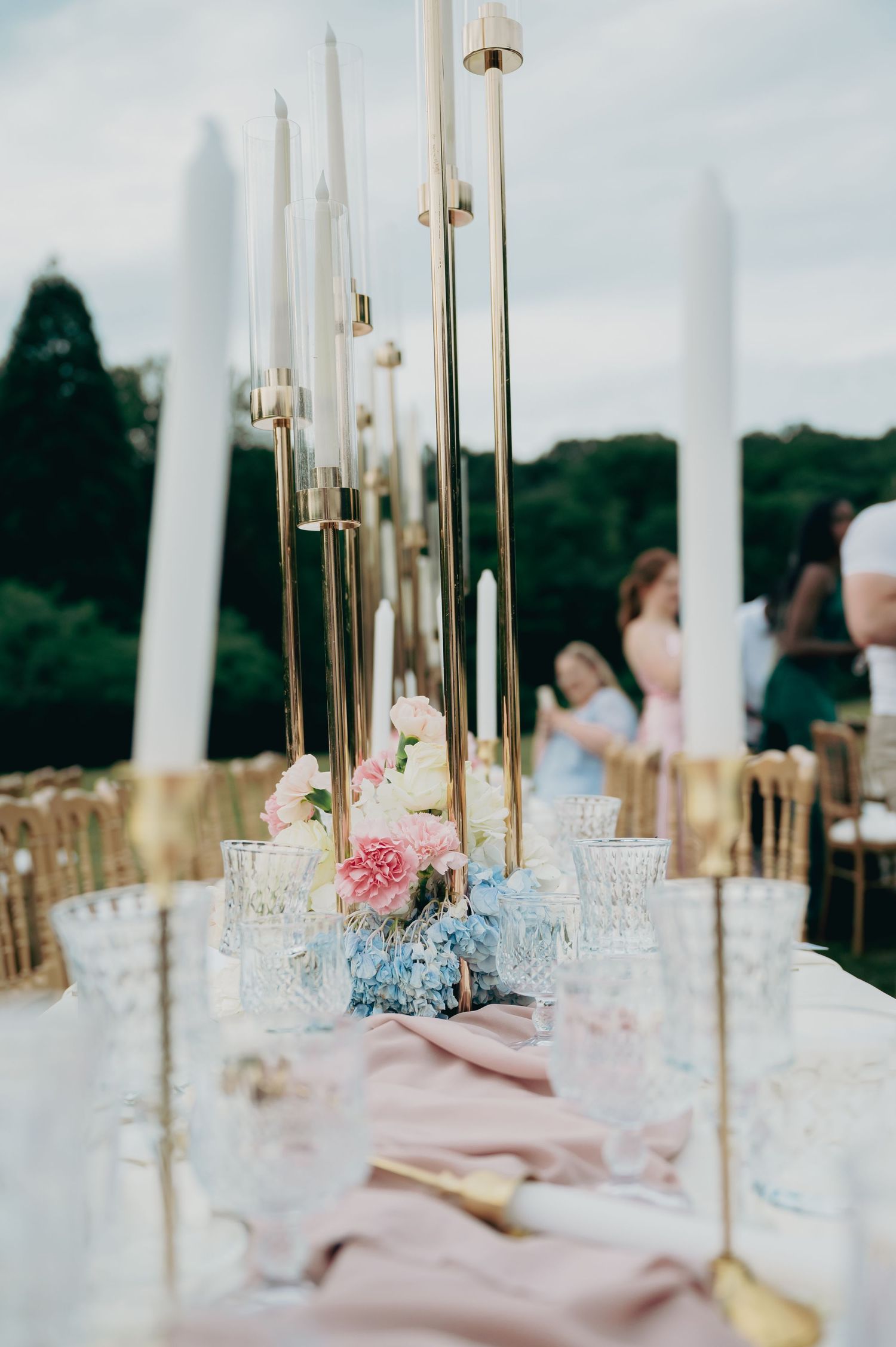 Outdoor wedding reception tablescape with gold candelabras, crystal glassware, and pink floral centerpieces.