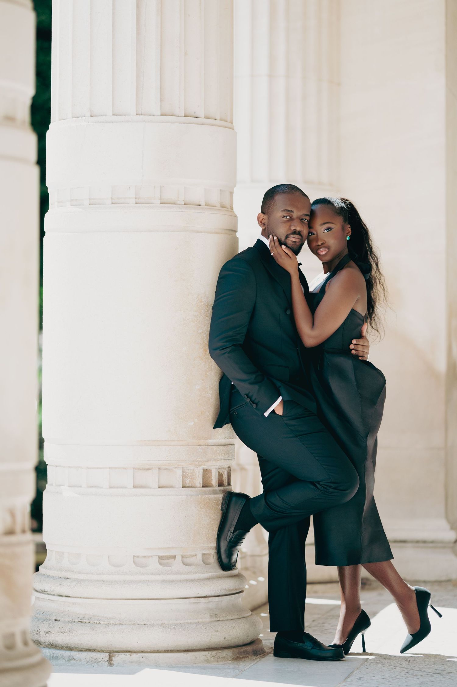 Stylish Black couple in black formal wear posing together against white classical architectural columns.