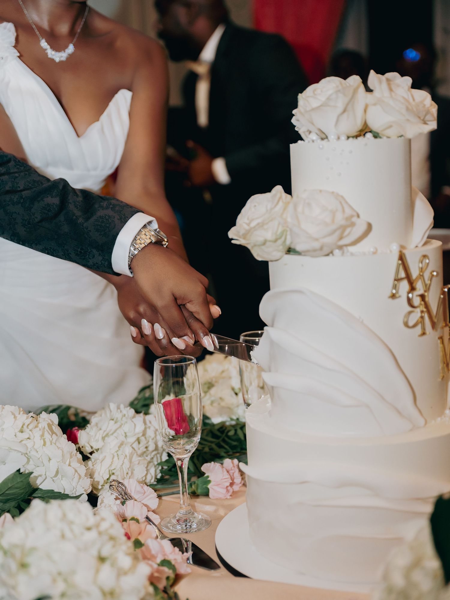 Bride and groom cutting a white tiered wedding cake adorned with roses and monogram initials at their reception.