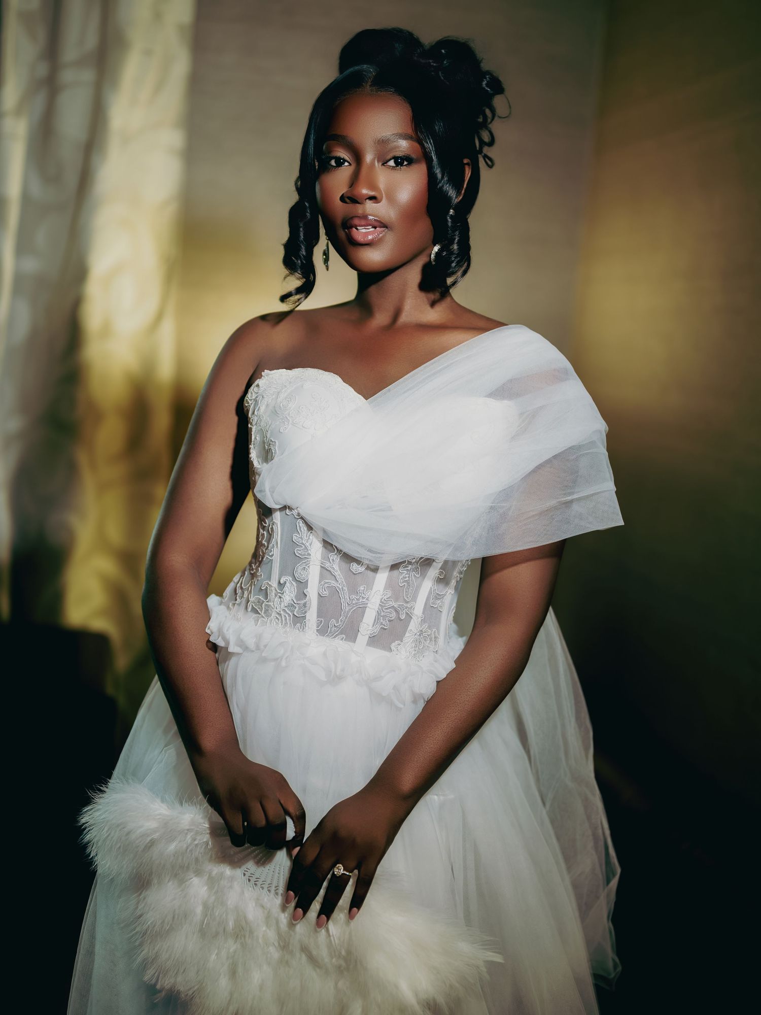 Stunning Black bride in white off-shoulder tulle corset gown holding a feather fan accessory.