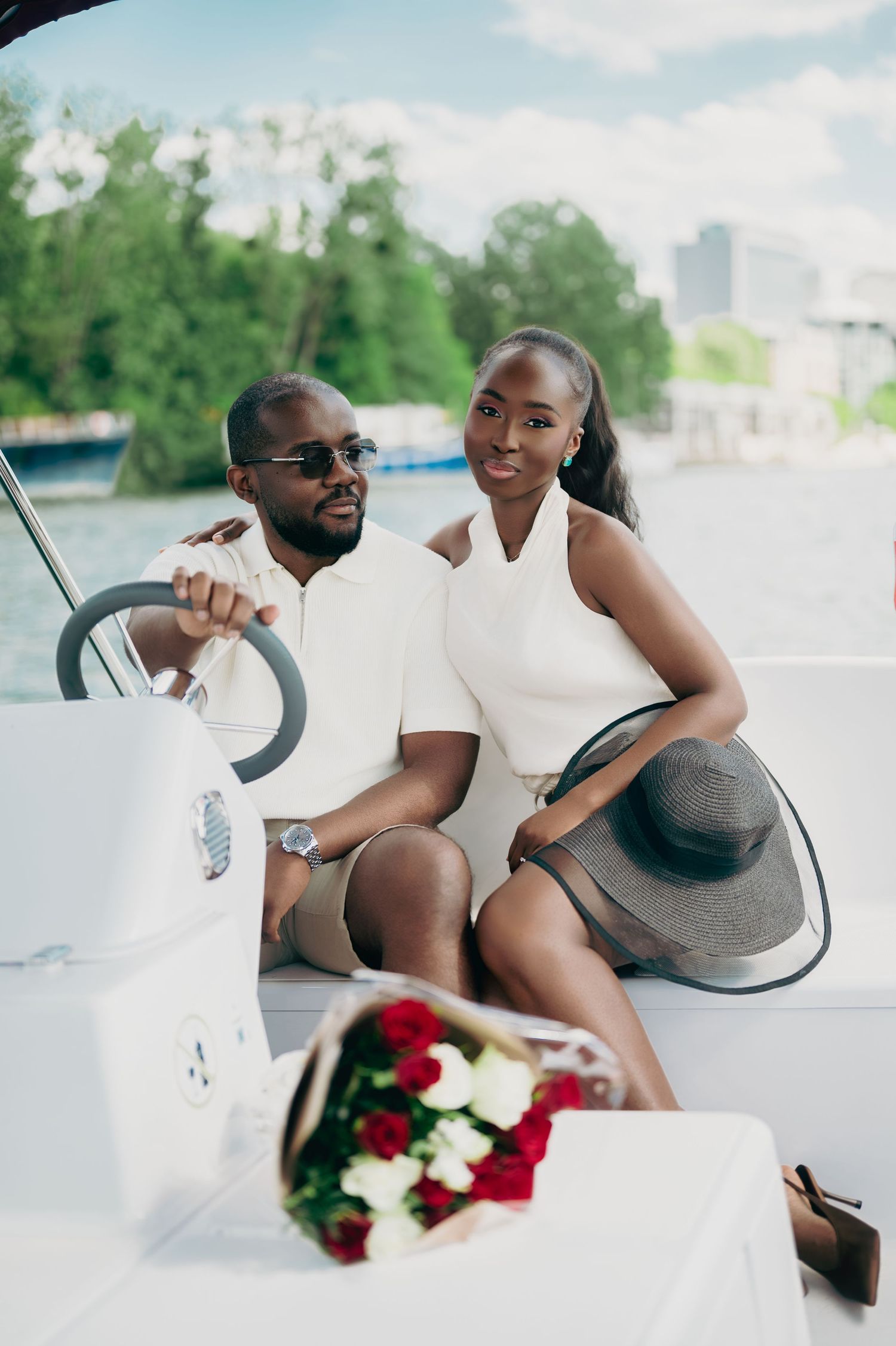 Relaxed Black couple in white casual outfits enjoy a romantic boat ride with red roses.