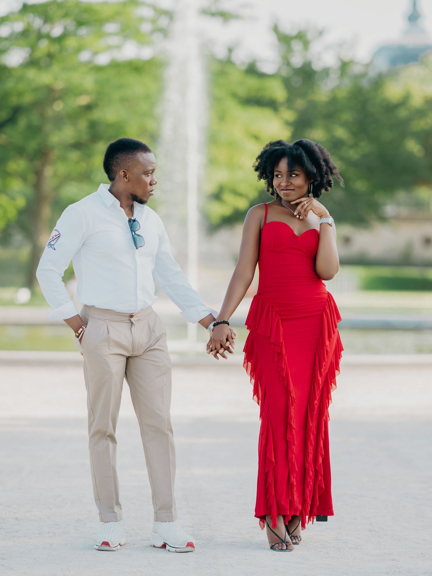 Black couple holding hands outdoors, woman in stunning red fringe gown and man in white shirt and khaki trousers.