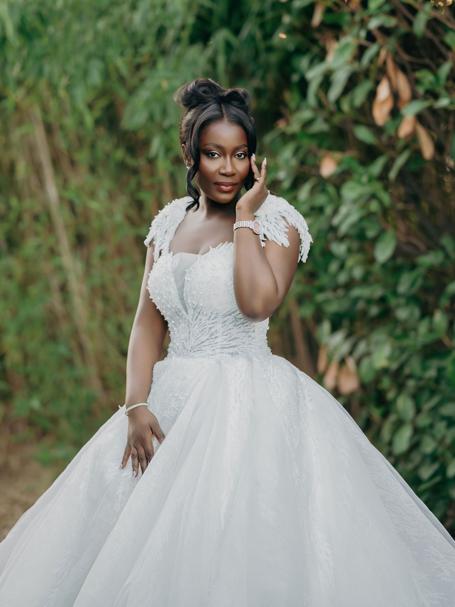 Beautiful bride in feathered white ball gown poses gracefully before a bamboo backdrop.