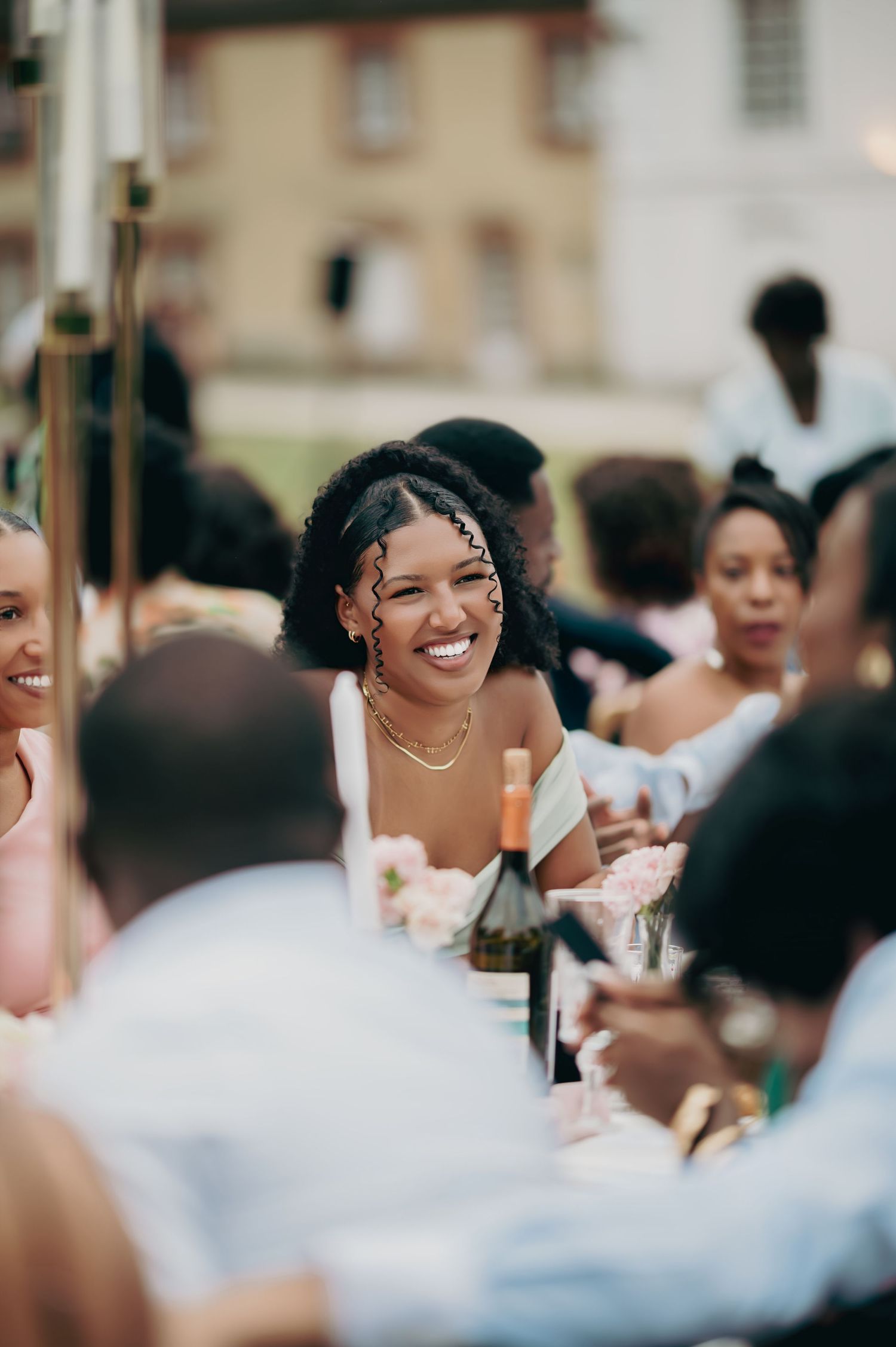 Smiling wedding guest with natural curly hair enjoys outdoor wedding reception dinner celebration.