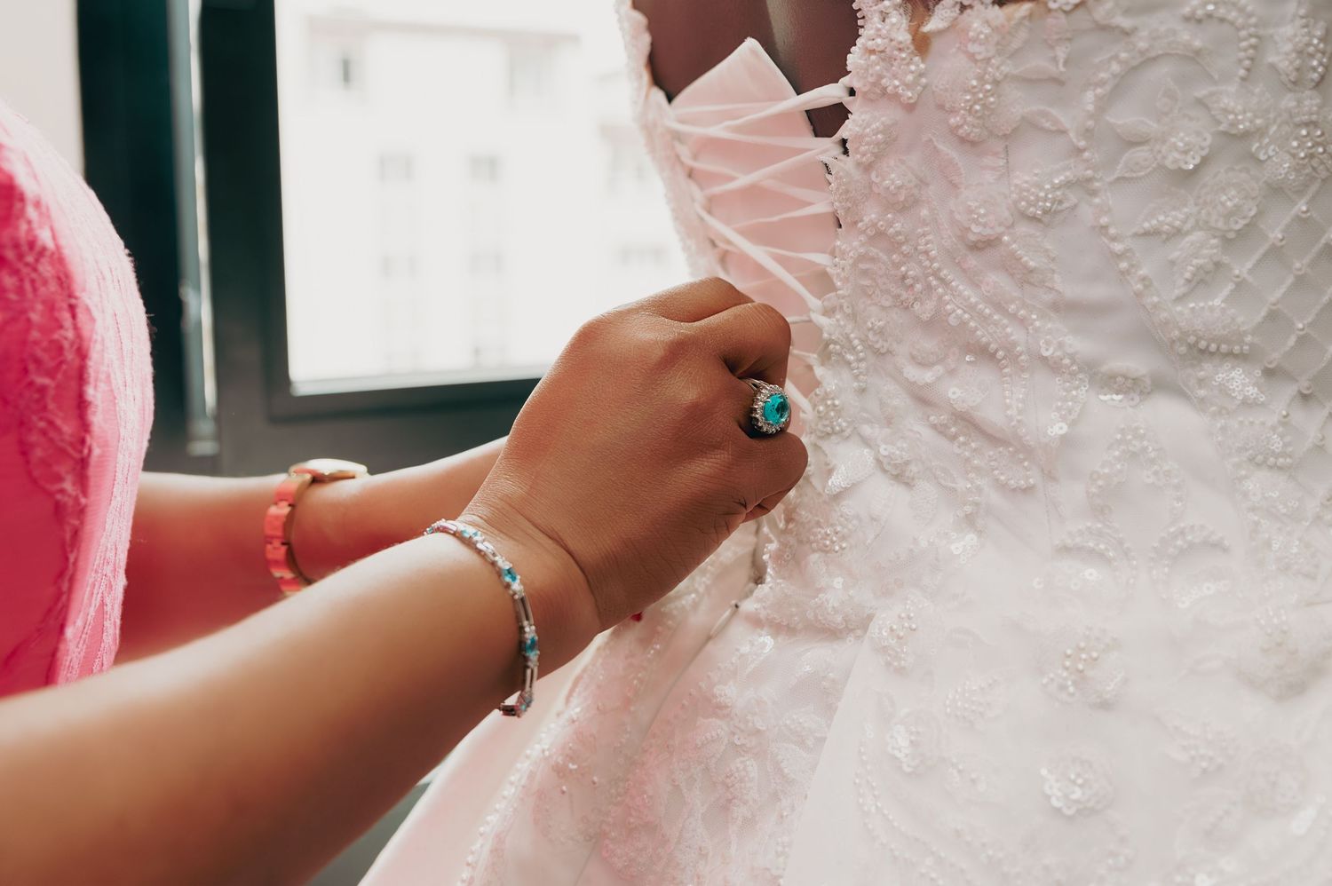 Bridesmaid fastening the lace corset back of a bride's intricate white wedding gown before the ceremony.