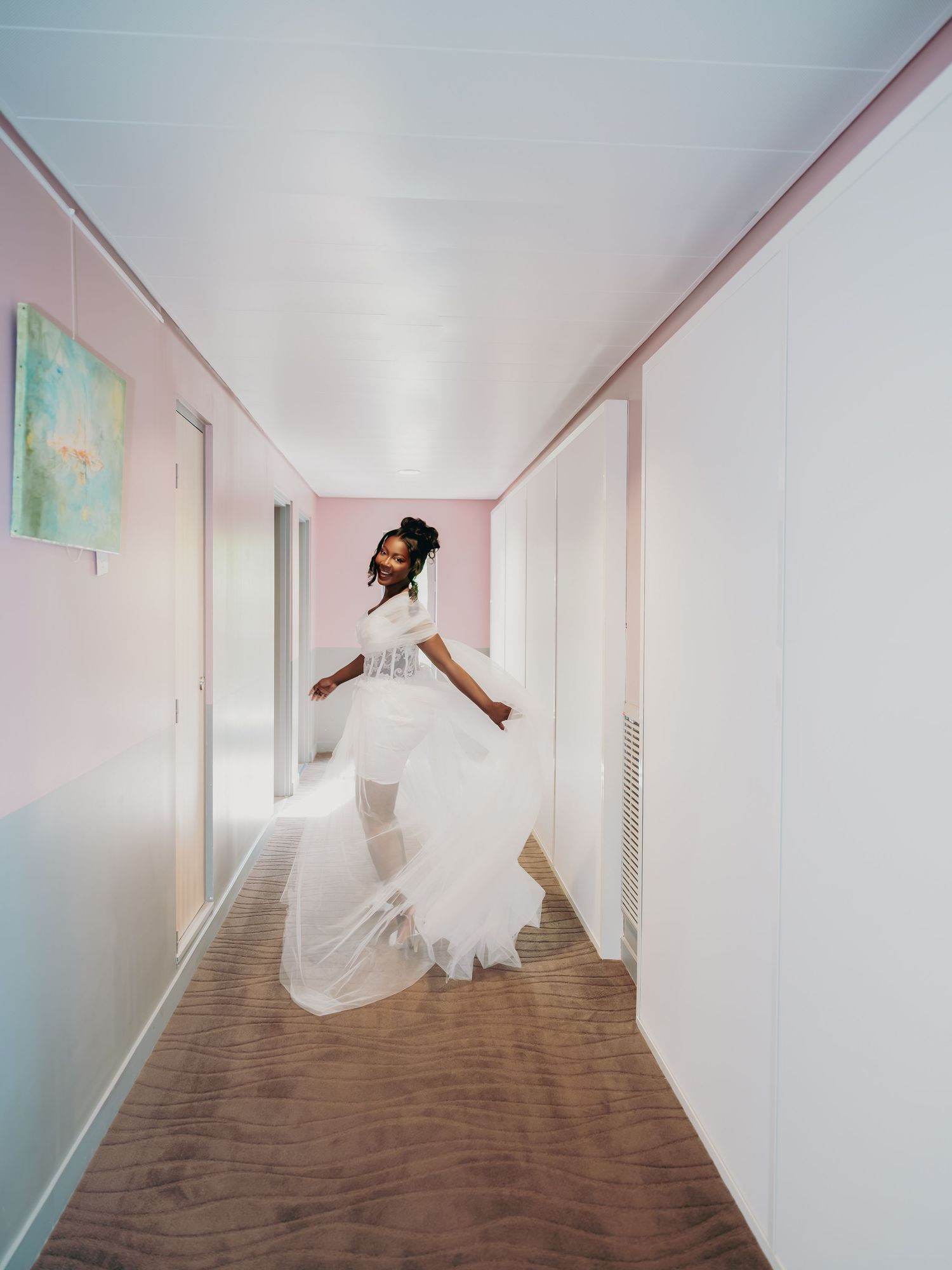 Bride in flowing white wedding gown twirling in a modern pink and white hallway.