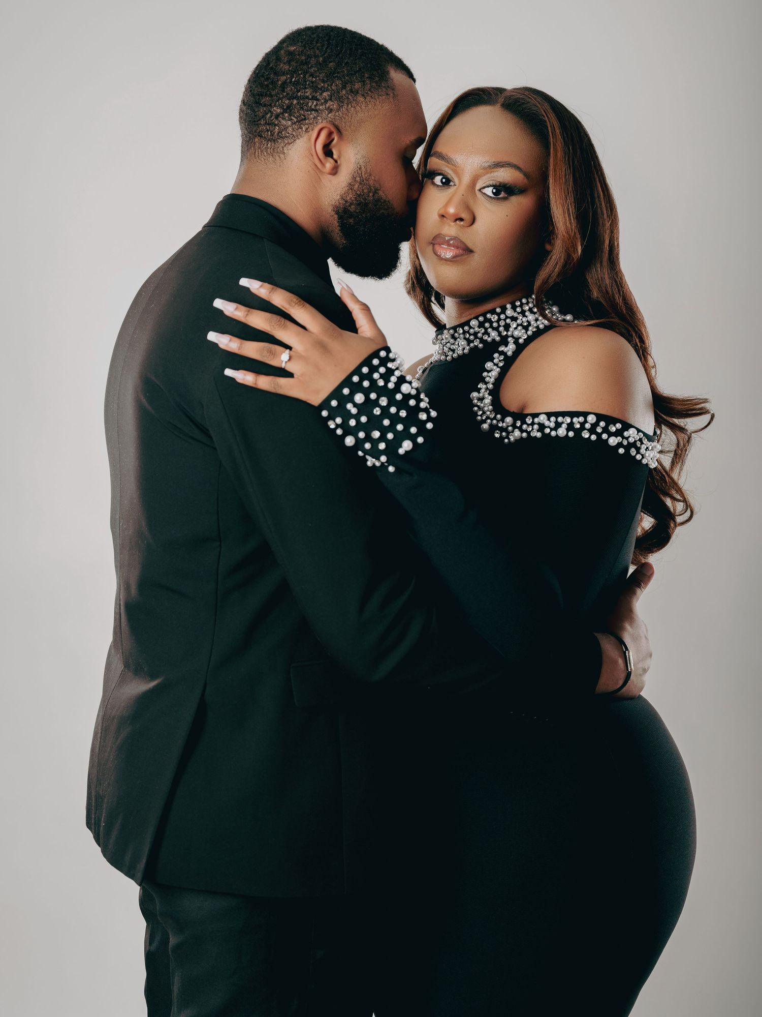 Couple in formal black attire share an intimate embrace in a professional studio setting.