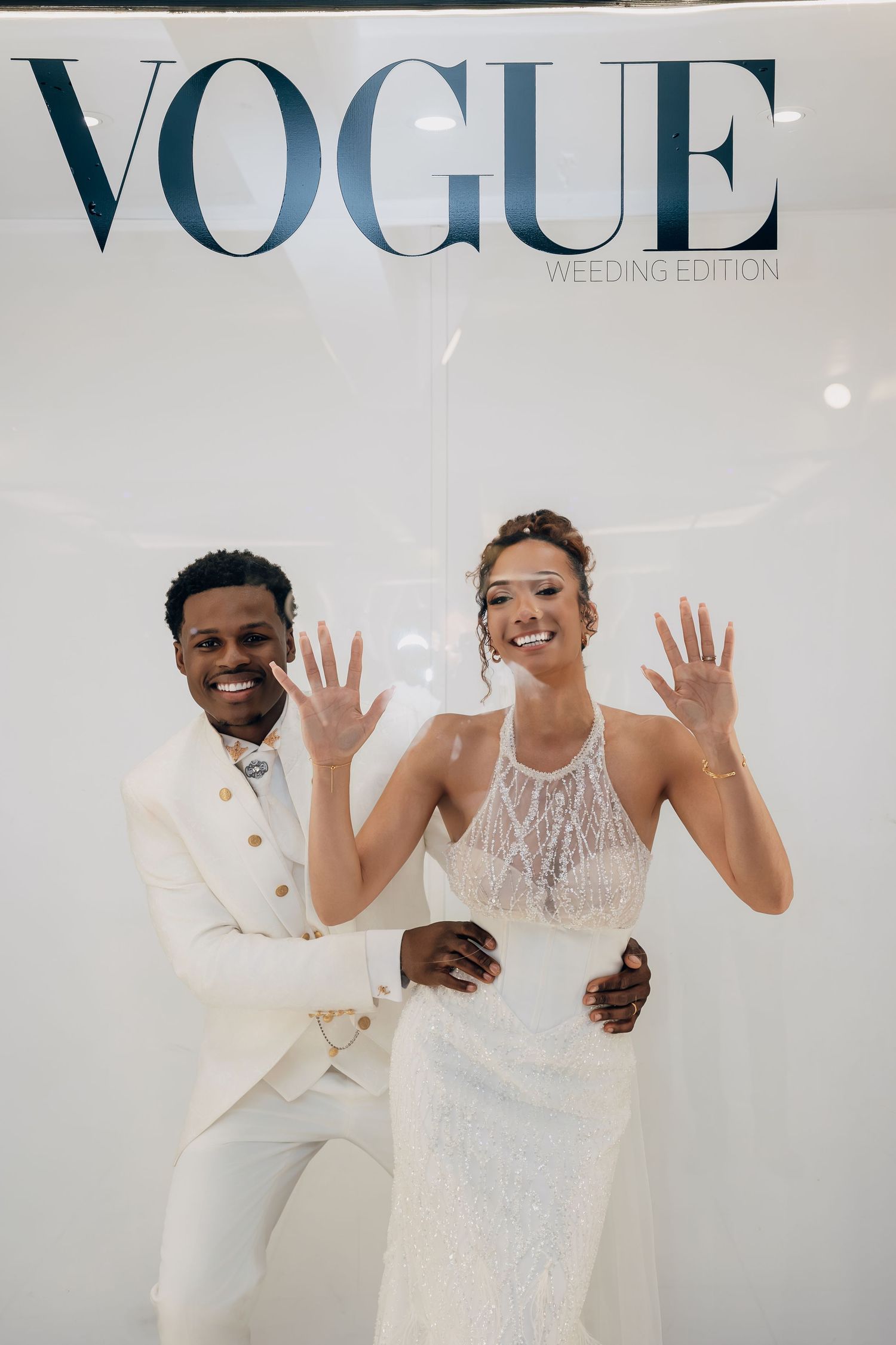 Smiling newlyweds posing in front of a Vogue Wedding Edition backdrop.