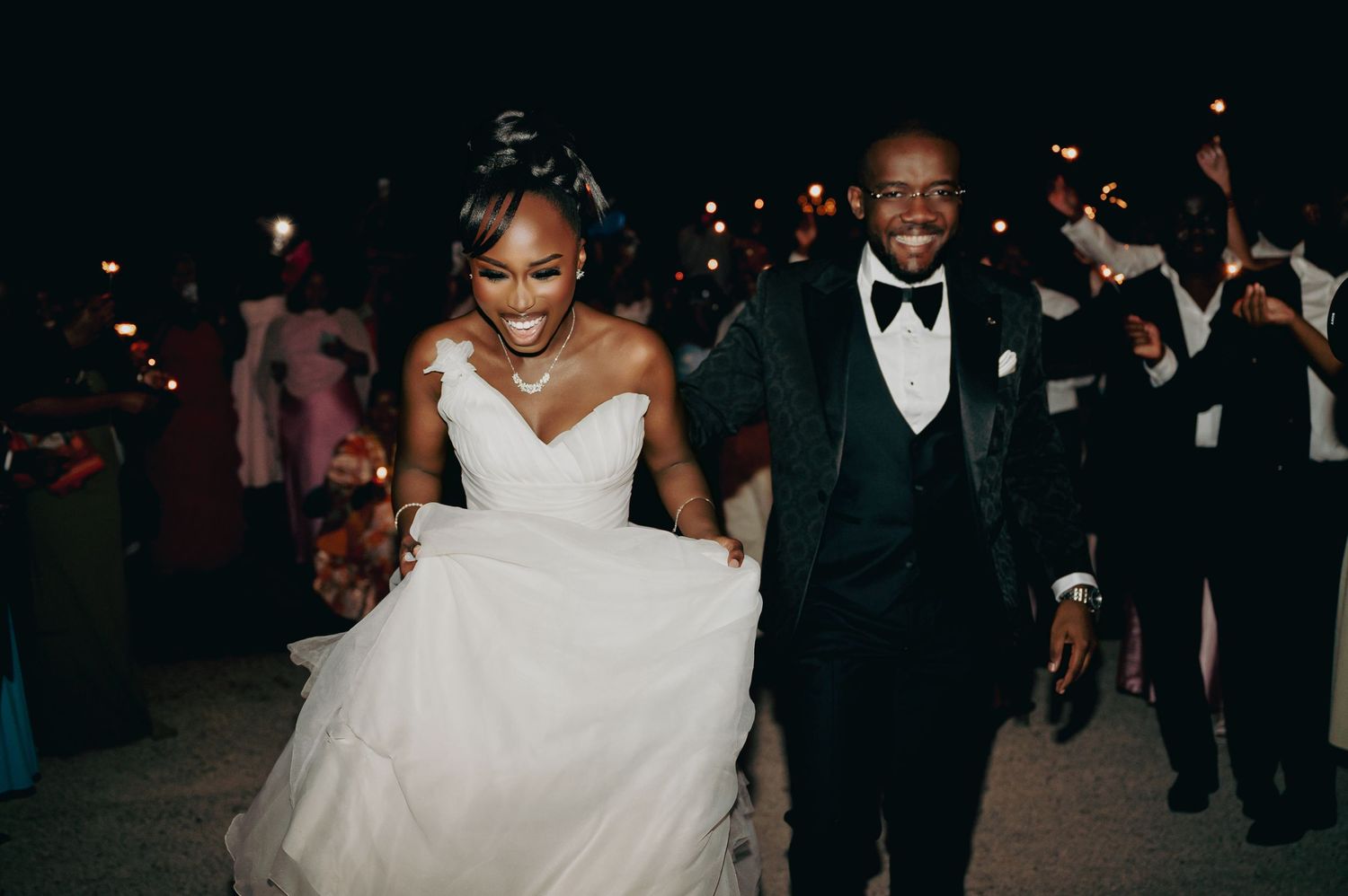 Joyful newlyweds making grand exit at night surrounded by guests holding sparklers.