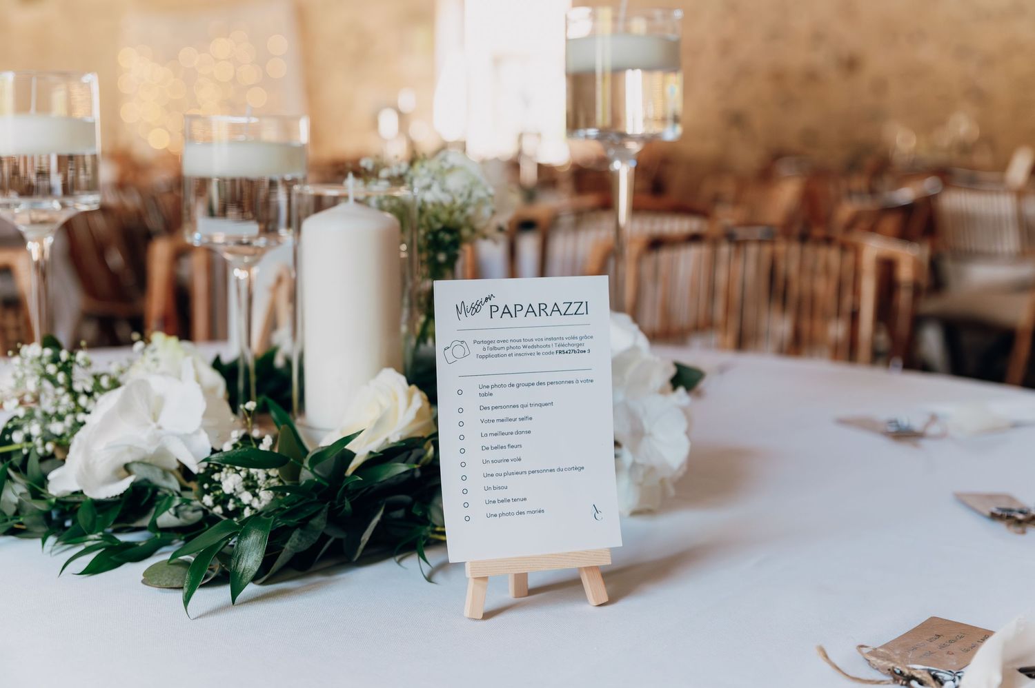 Elegant wedding table centerpiece with white roses, greenery, candles, and a paparazzi table sign.