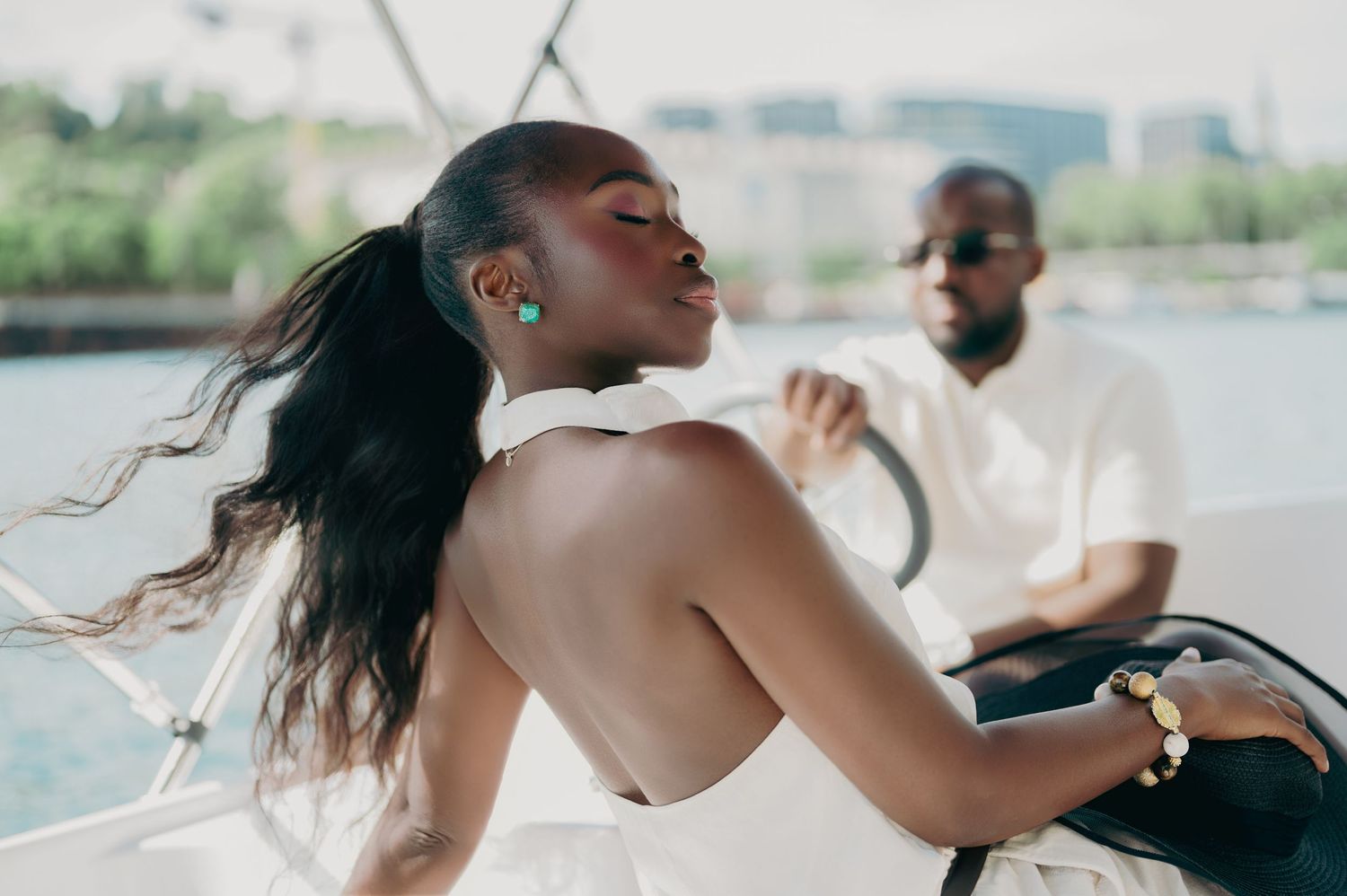 Young Black woman with long ponytail in white dress on a boat, man in white shirt in background.