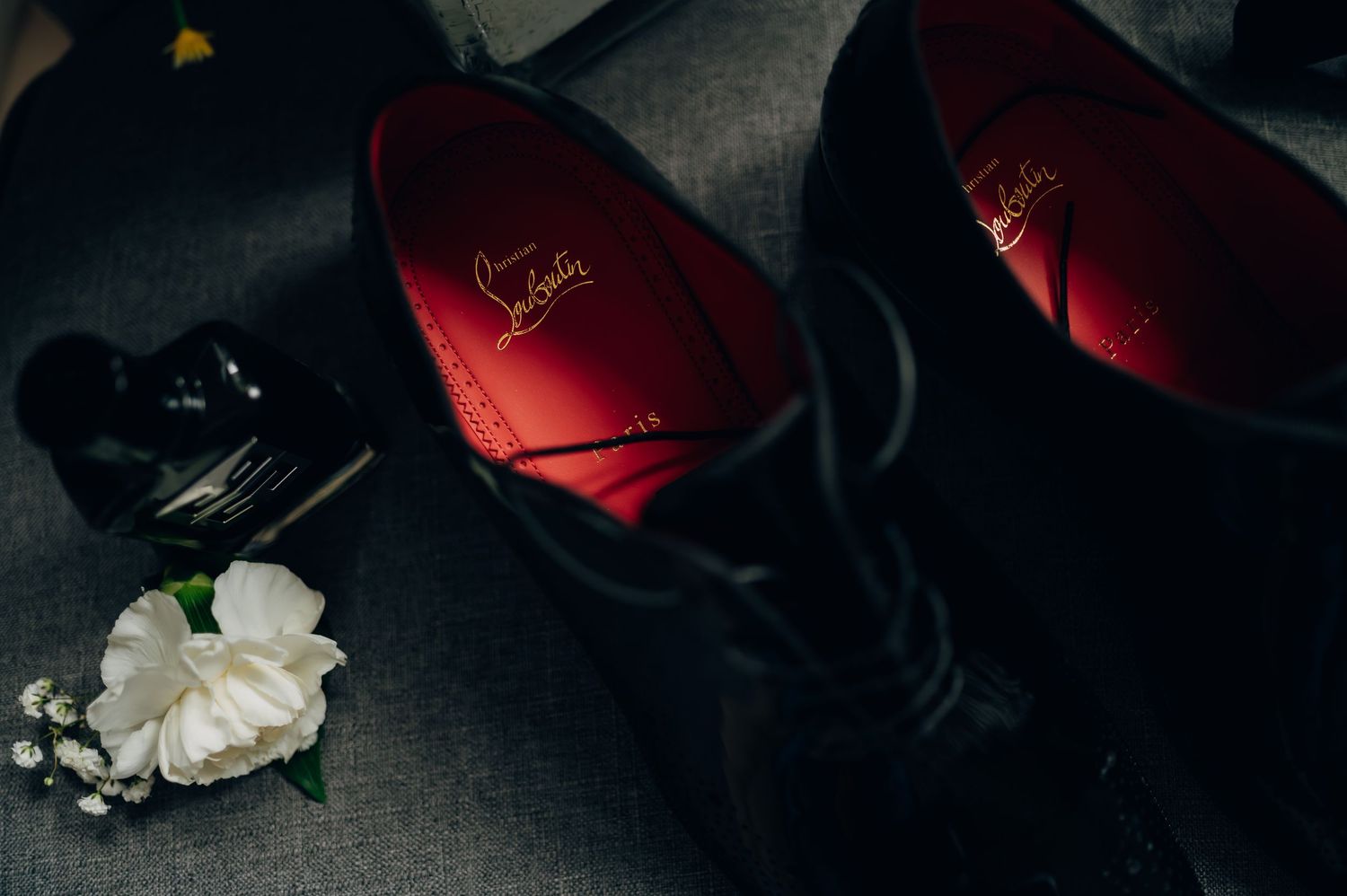 Christian Louboutin black dress shoes with red soles beside a white floral boutonniere.