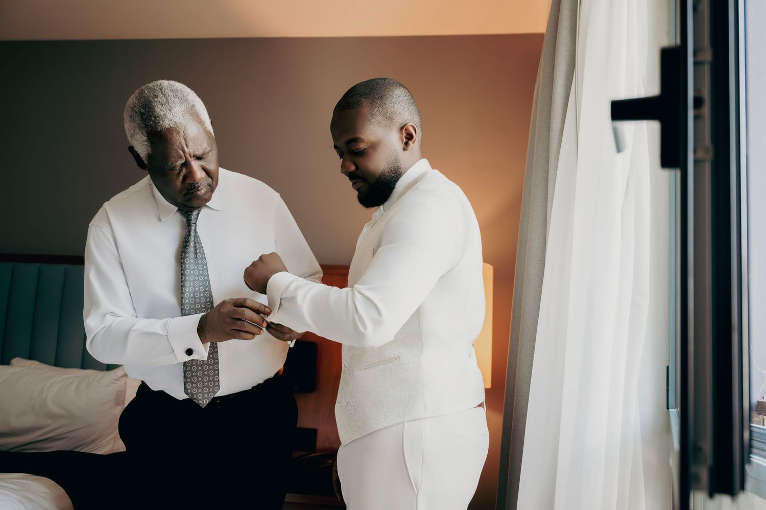 An older man and younger man in formal attire helping with cufflinks before a wedding.