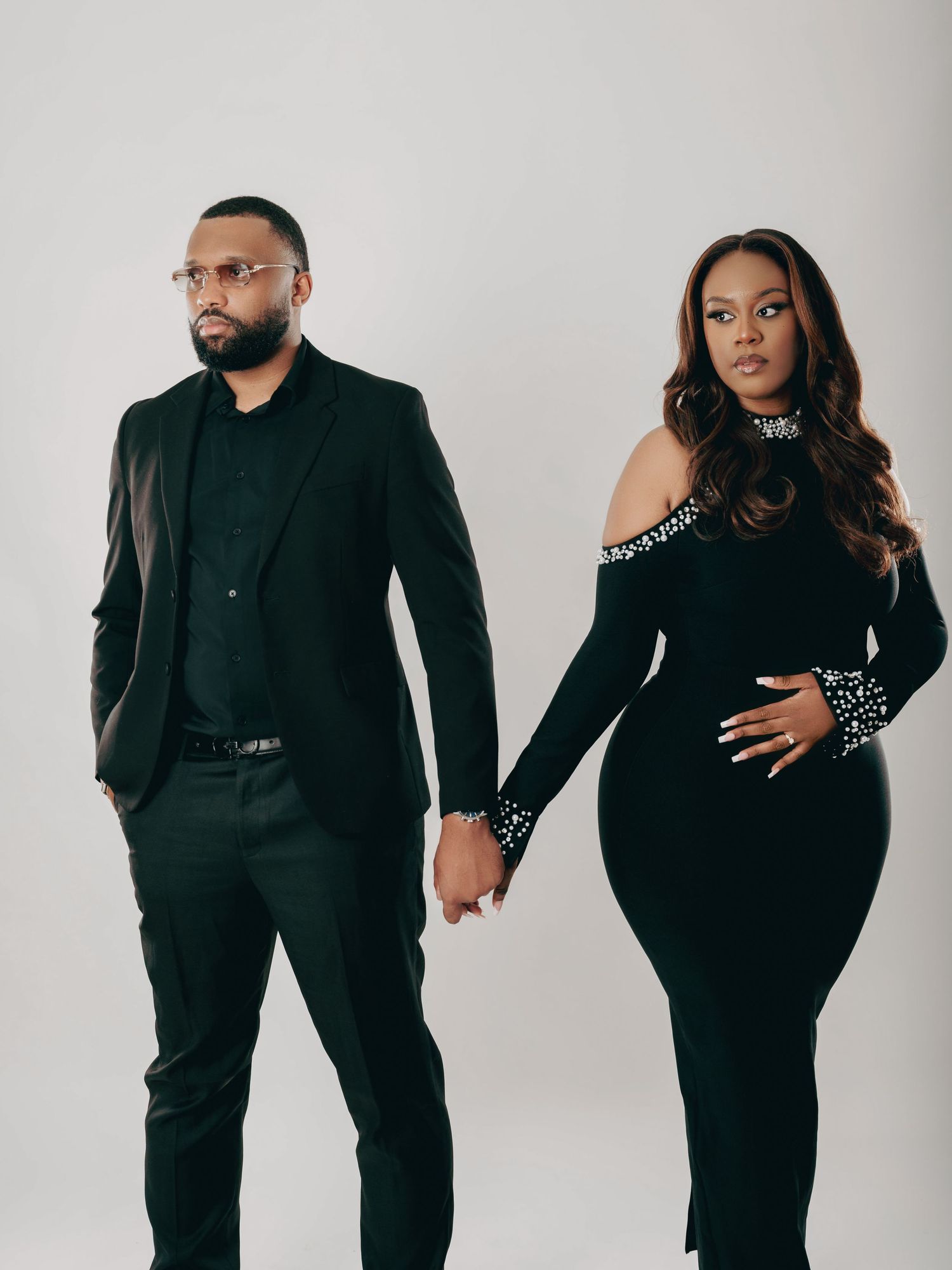 Stylish couple holding hands in coordinating black beaded formal wear for maternity photos.