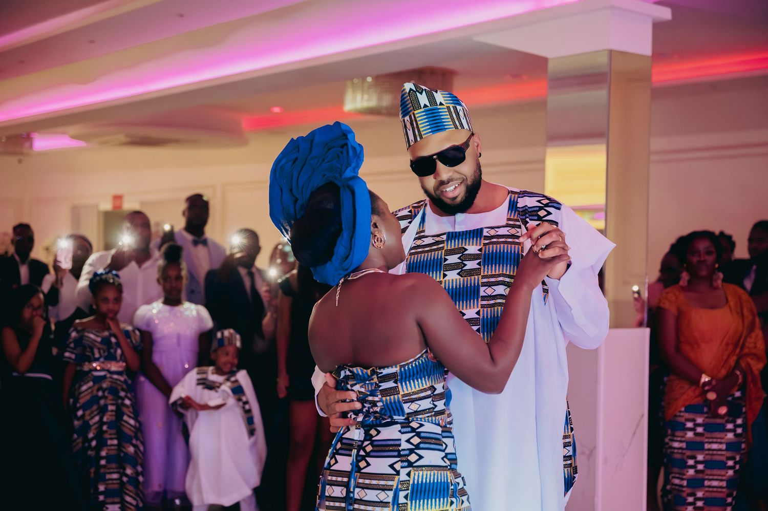 Bride and groom in traditional African kente attire share romantic first dance at wedding.