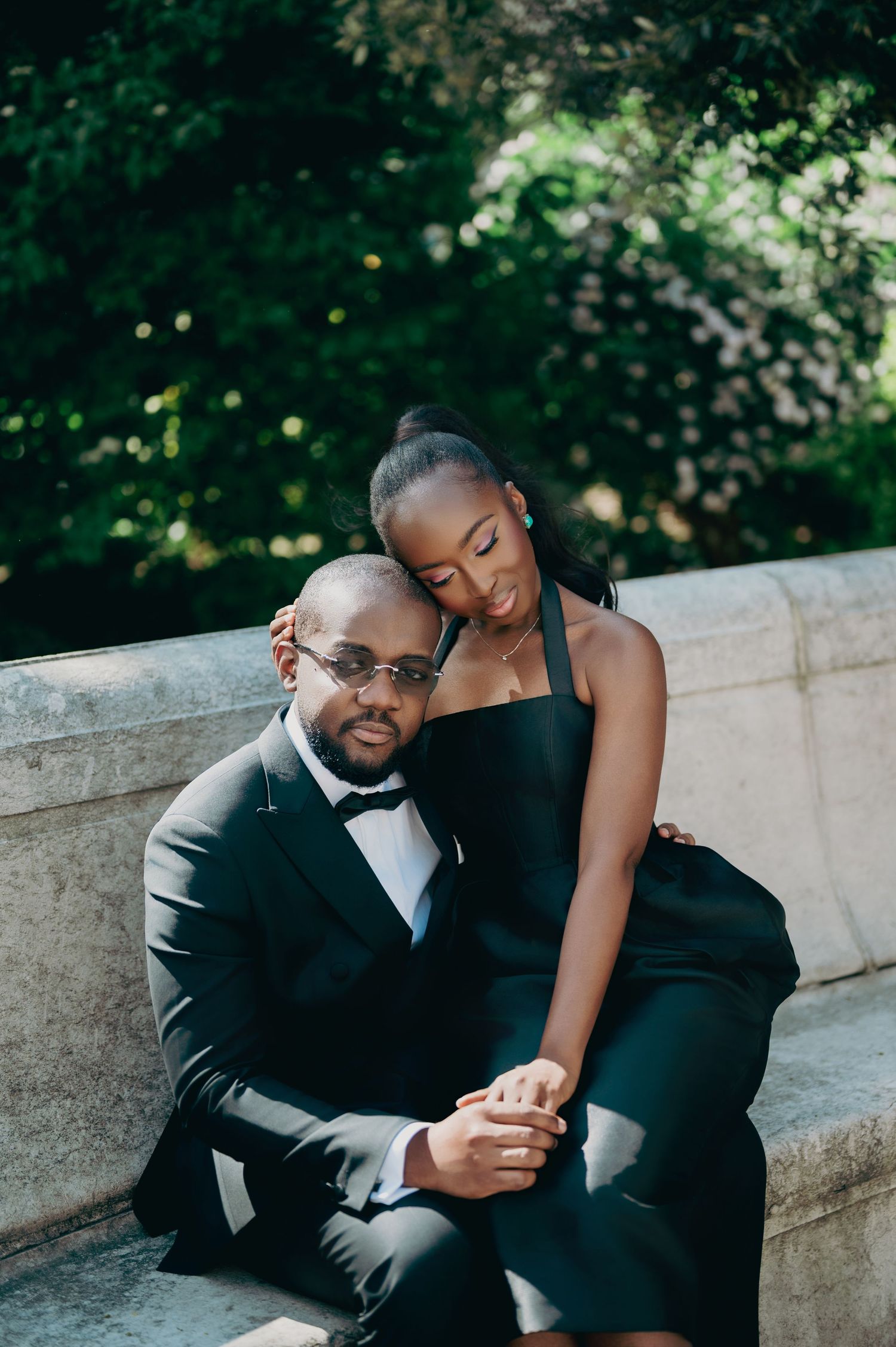Affectionate Black couple in black formal wear cuddle closely on sunlit stone steps.