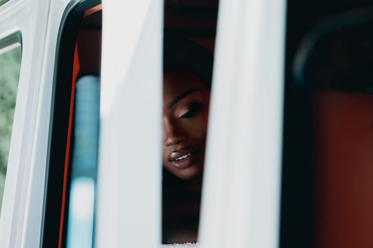Smiling Black woman seen through white window frame, captured in a candid portrait.