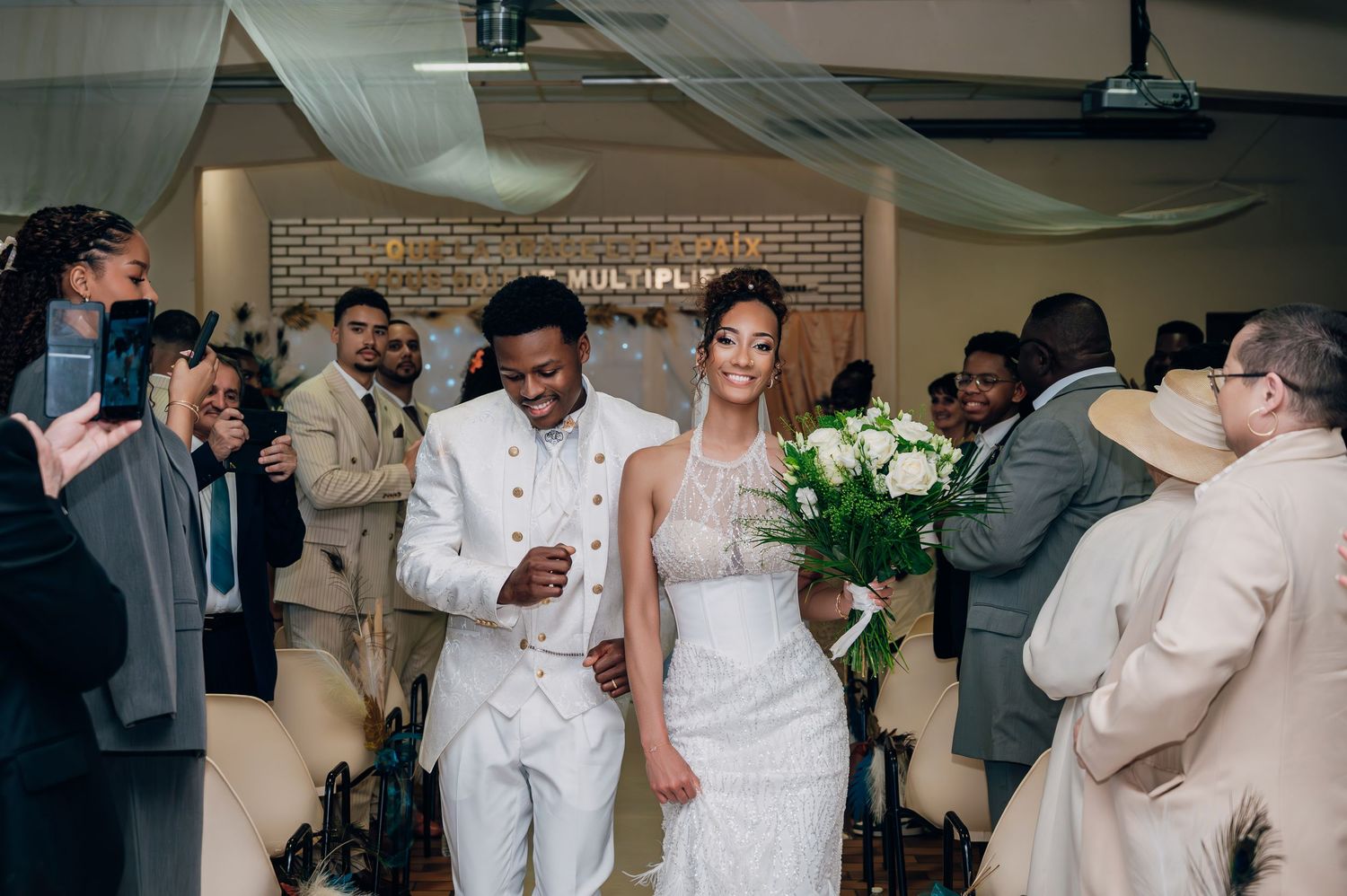 Newlywed couple walks down the aisle after ceremony surrounded by cheering wedding guests.