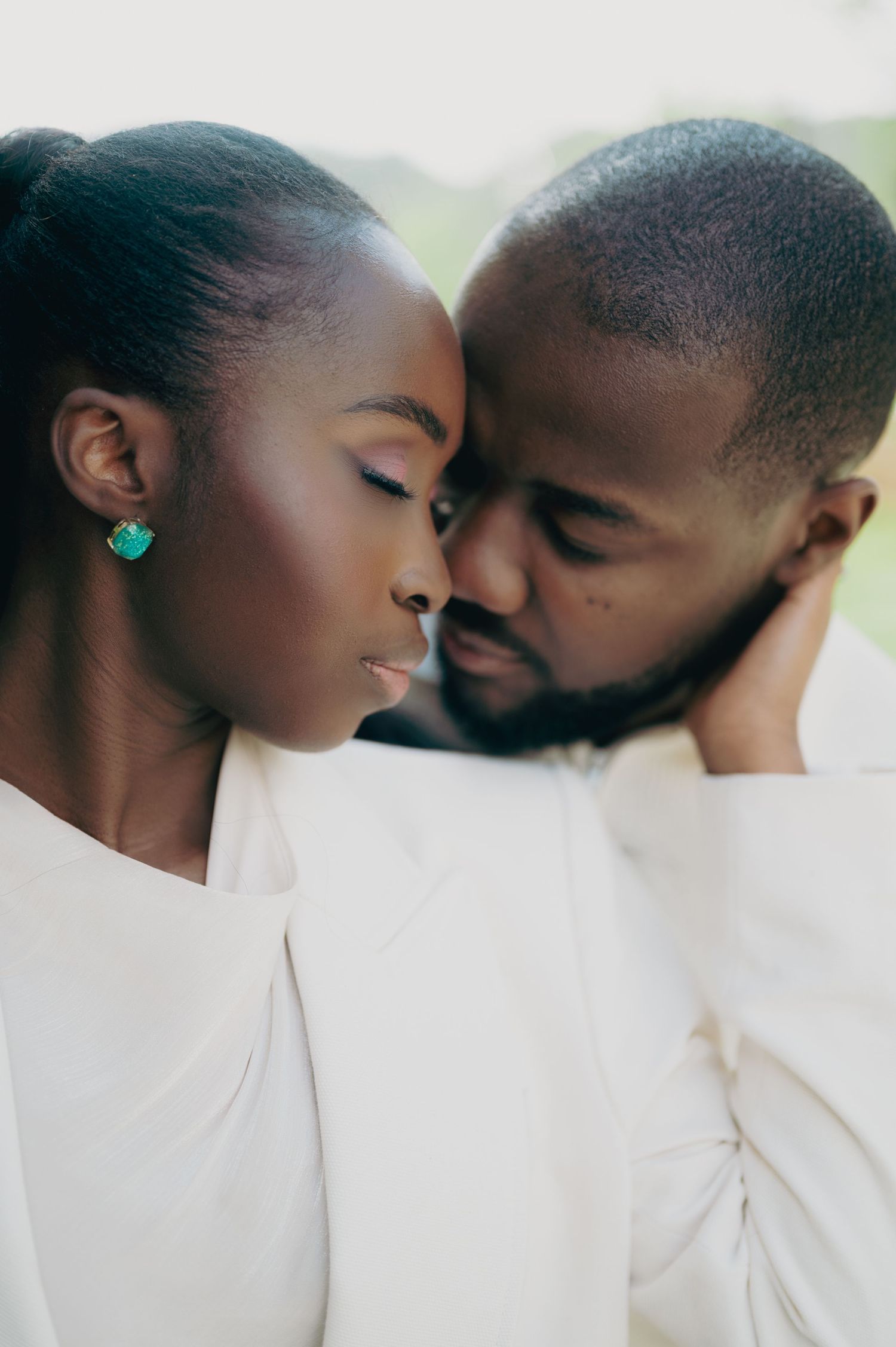 A close romantic moment between a couple touching foreheads, with the woman wearing a teal earring.