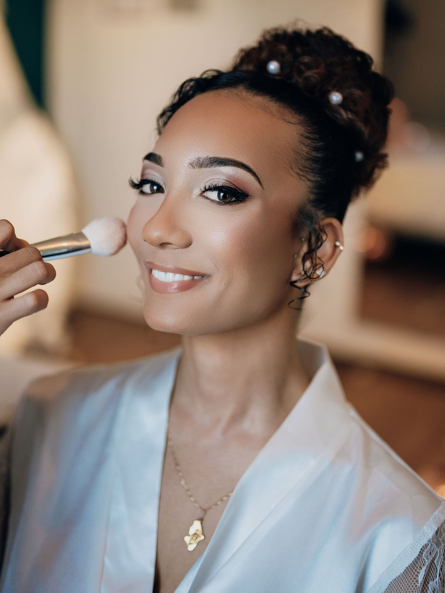 Bride getting makeup applied with pearl hair accessories and updo hairstyle.