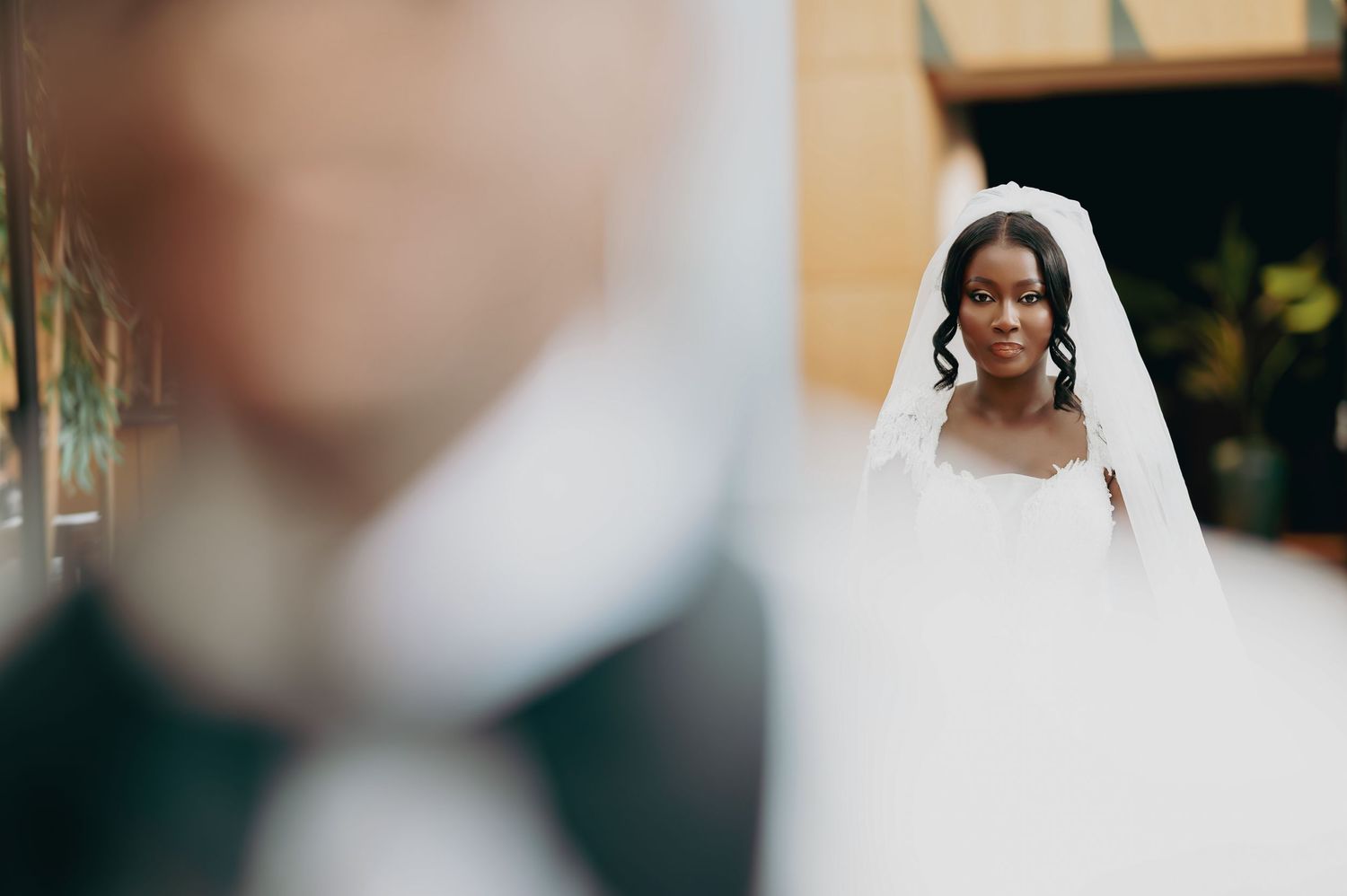 Black bride in white wedding dress and veil walking toward groom in a softly blurred romantic photo.