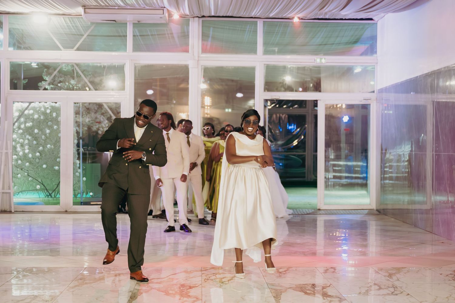Wedding guests dancing joyfully on marble dance floor during elegant indoor reception celebration.