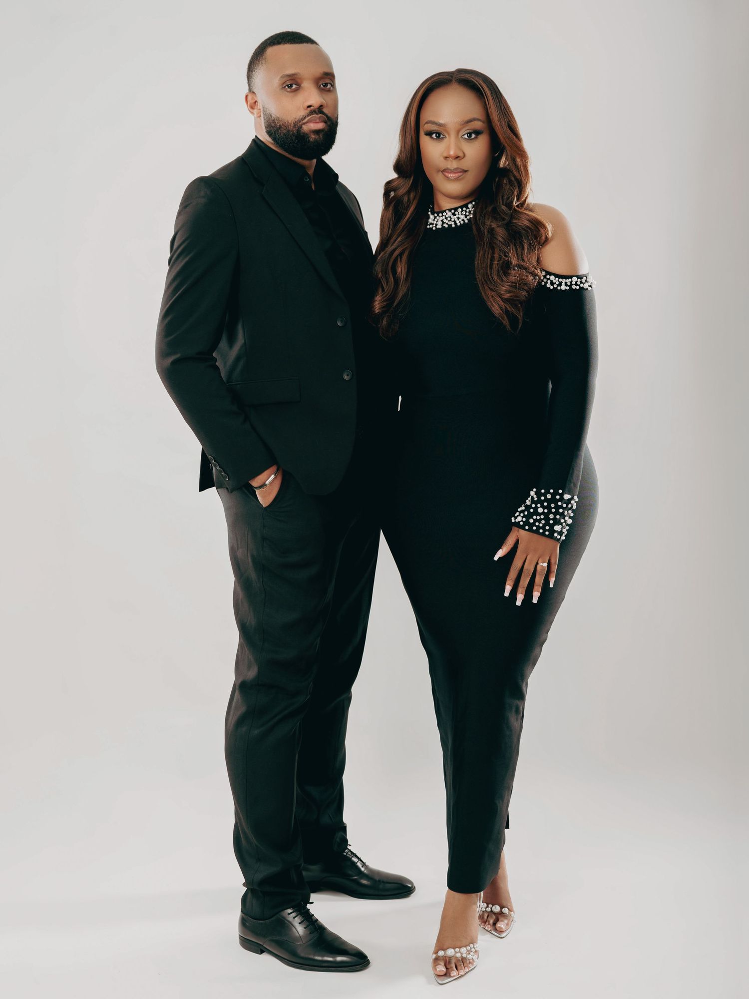 Fashionable couple standing together in coordinated black formal outfits during a professional photo session.