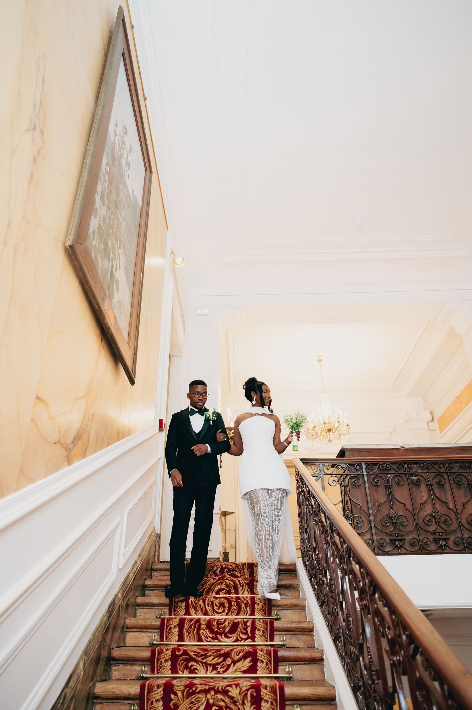 Bride and groom sharing a romantic moment on a grand staircase with red carpet and ornate railing.