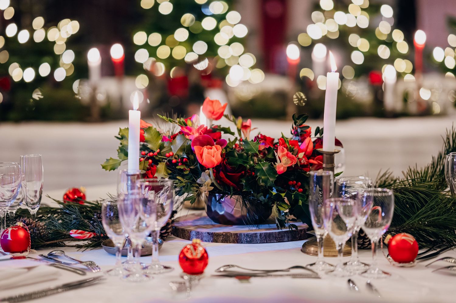 Festive Christmas wedding table setting with red roses, white candles, pine branches, and ornament decorations.