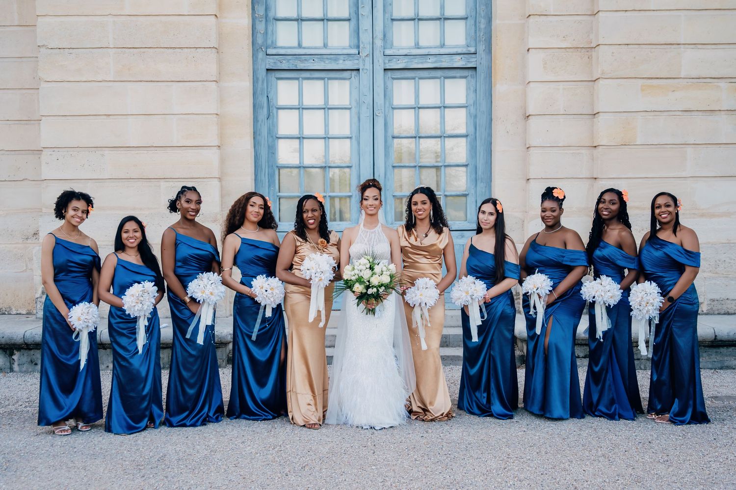Bride poses with bridesmaids in elegant royal blue satin gowns holding white bouquets.