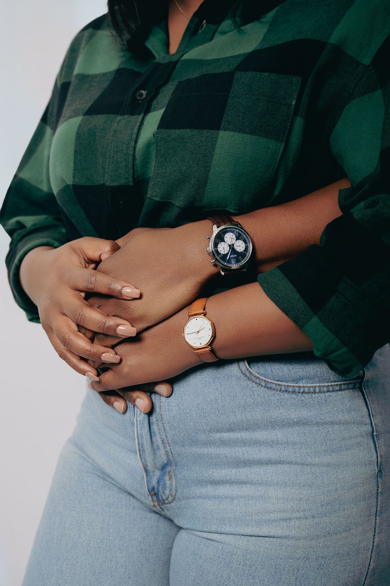 Close-up of a woman wearing two watches on her wrists, dressed in a green plaid shirt and light blue jeans.