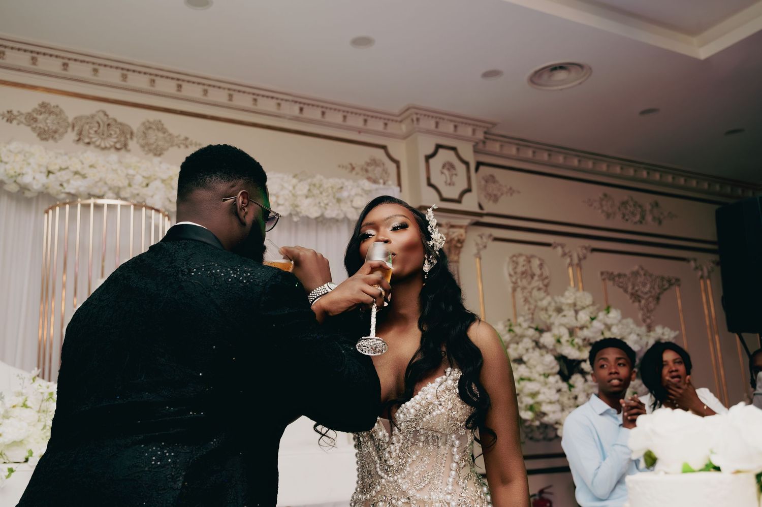 Bride and groom sharing a champagne toast at an elegant wedding reception with white floral decor.