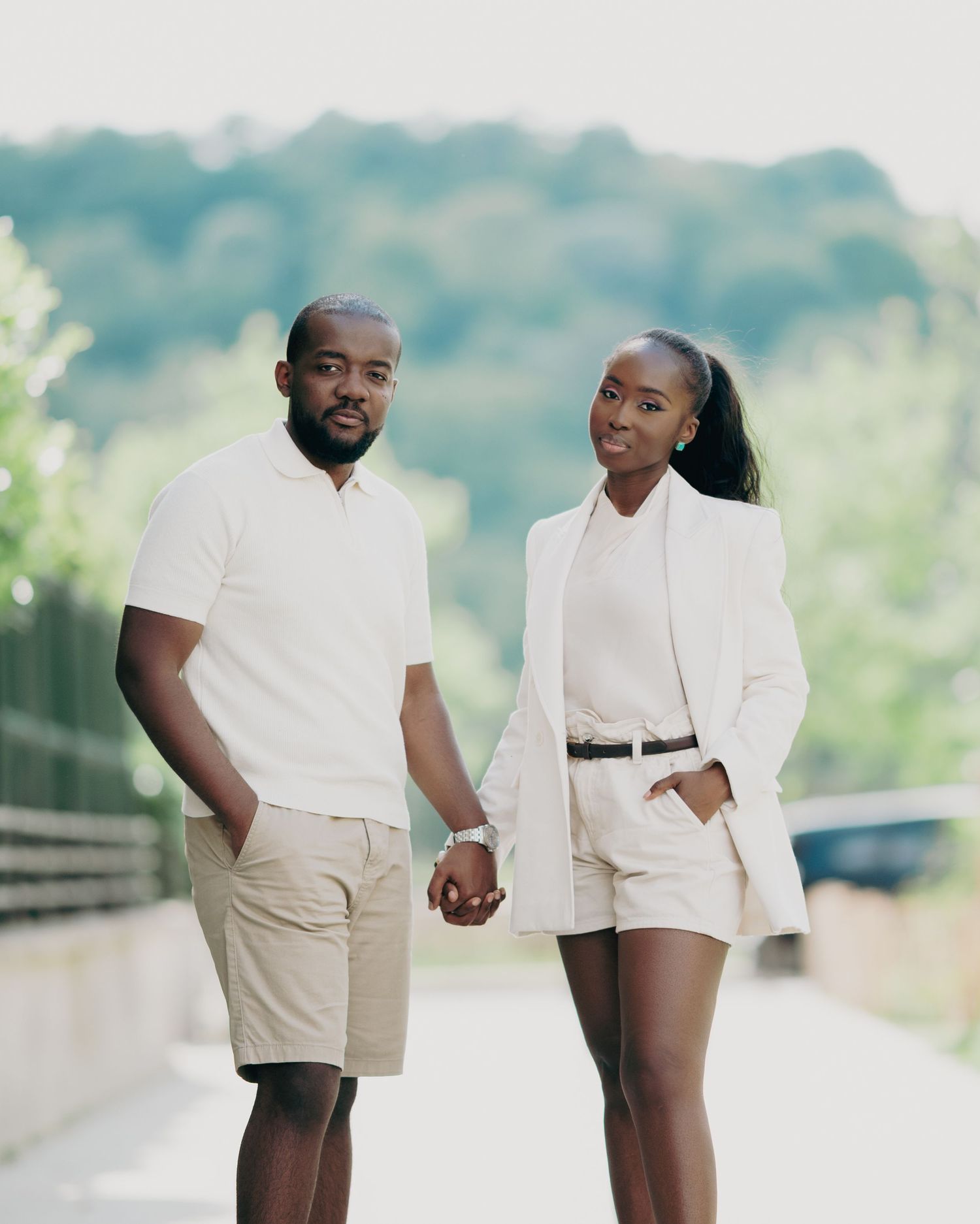 Stylish Black couple holding hands outdoors in matching white and beige outfits on a sunny day.