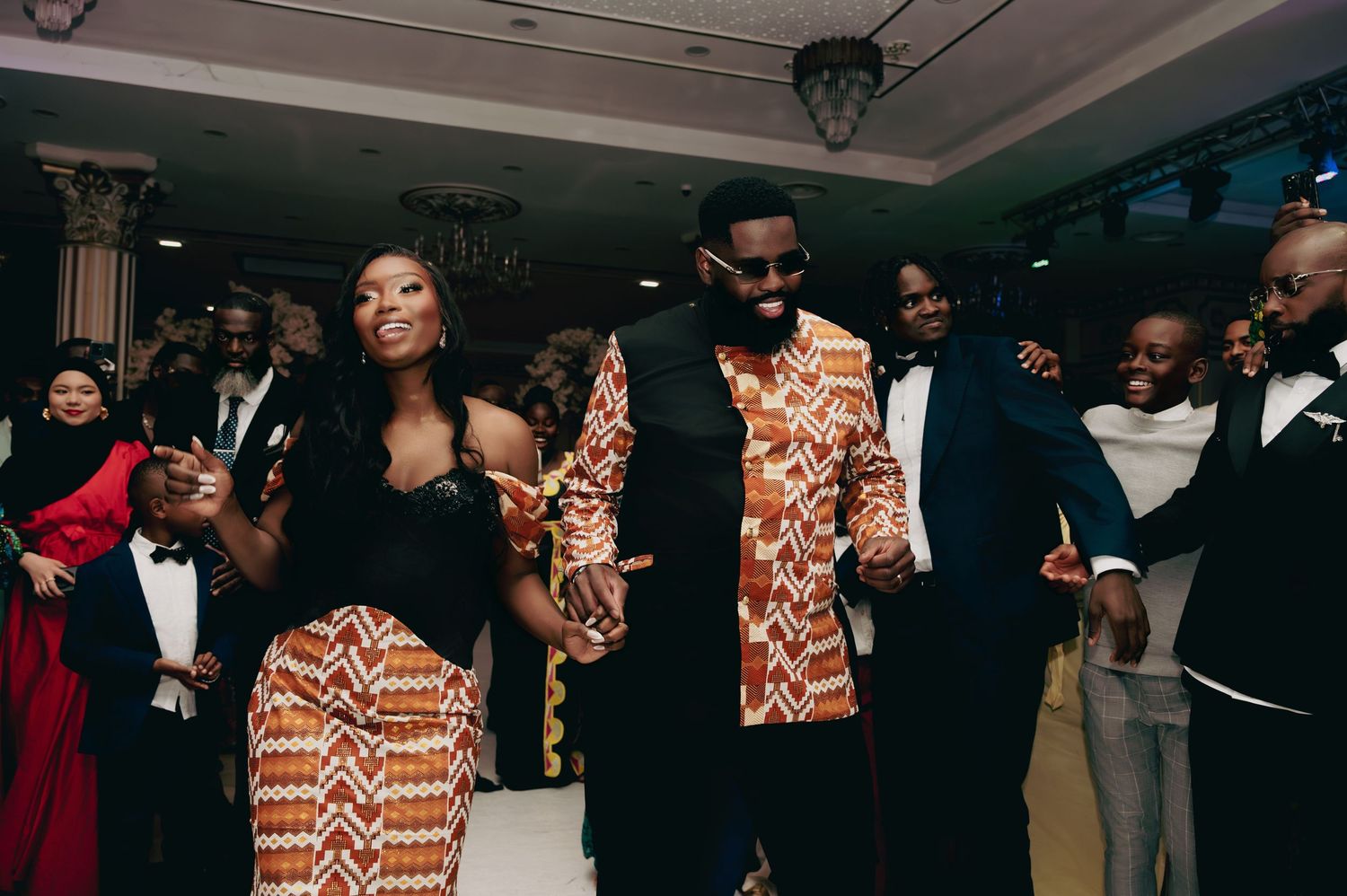 Couple dancing joyfully in traditional African kente attire at a vibrant wedding reception celebration.