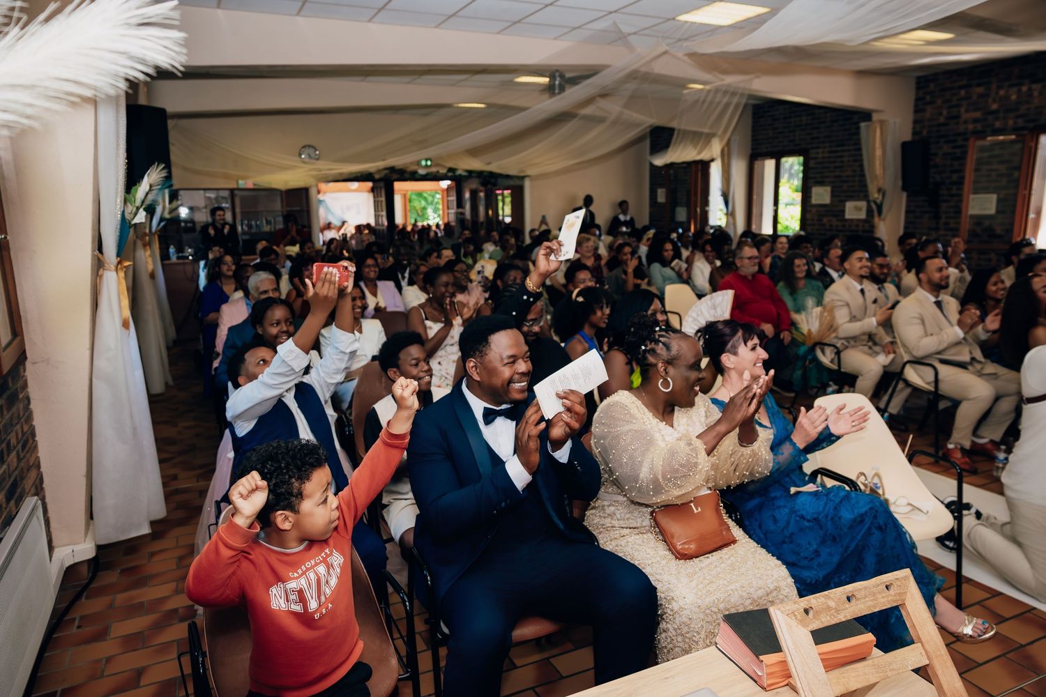 Wedding guests enthusiastically wave envelopes and celebrate at lively indoor reception.