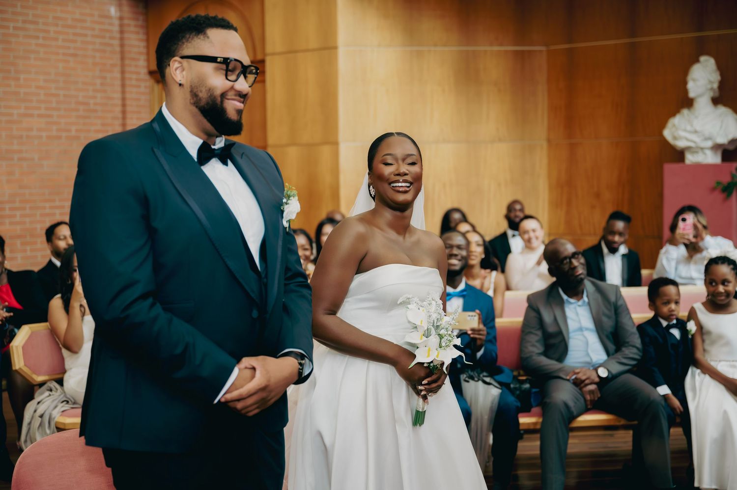Smiling couple walks down the aisle during their wedding ceremony in a warmly lit ceremonial hall.