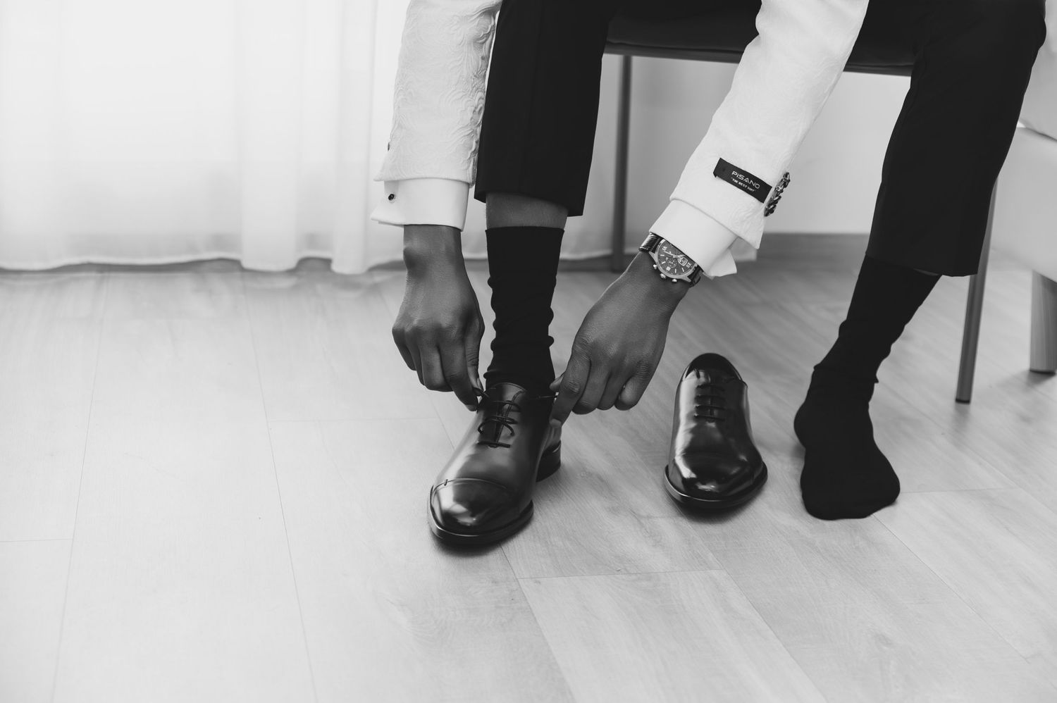 Black and white photo of groom tying his dress shoes while wearing a watch on his wedding day.